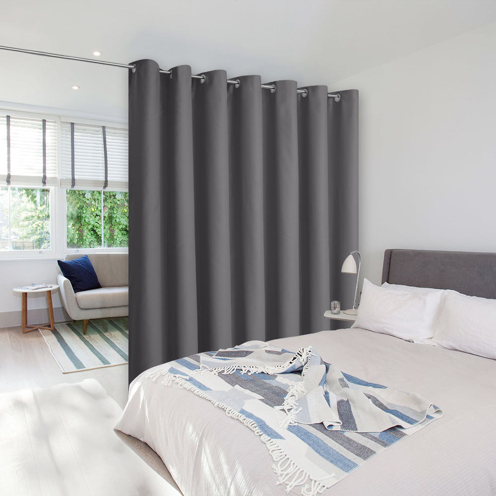A dark grey room divider curtain with grommets separating a modern bedroom from a sunlit living area.