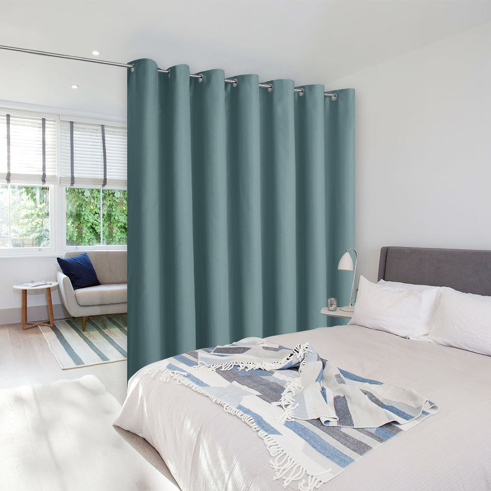 A teal room divider curtain with silver grommets partitions a bedroom area from a small living space.