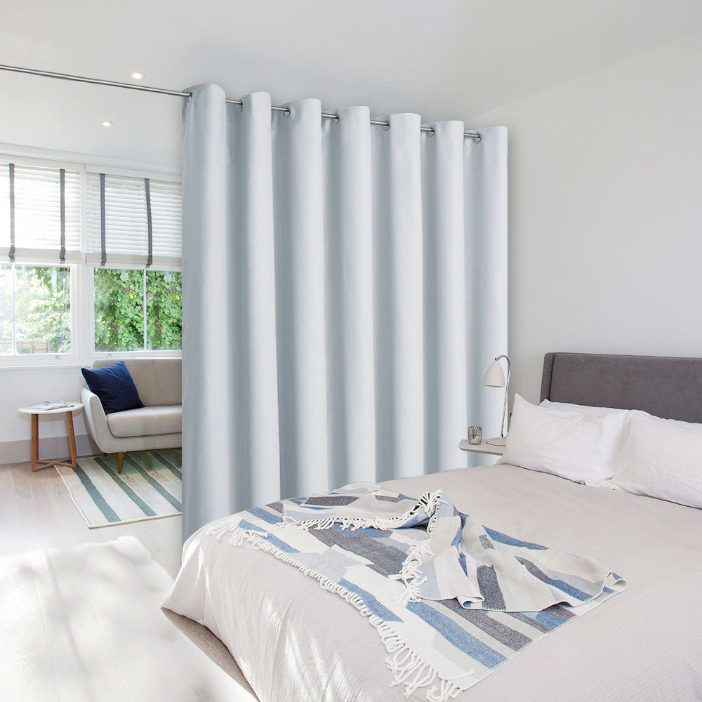 A light grey room divider curtain on a rod separates a bedroom from a living area, creating privacy in a modern home.