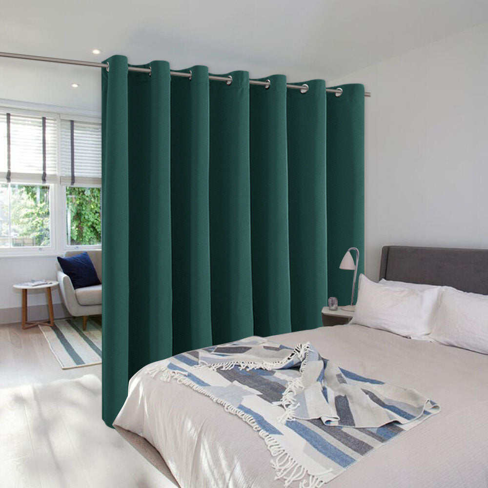 Dark teal room divider curtain with grommets separating a bed from a living area to create a private bedroom space.
