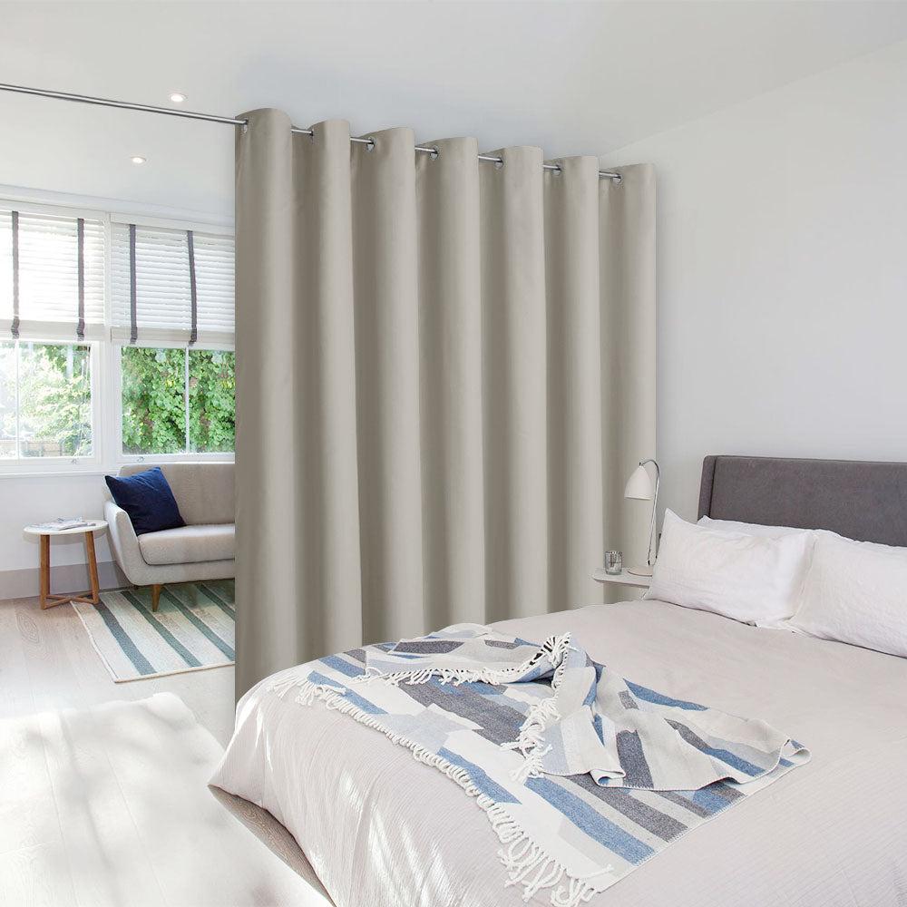 Beige room divider curtain with silver grommets on a tension rod separating a bedroom from a living room area.