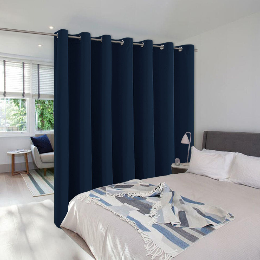 A long navy blue room divider curtain with silver grommets separates a bedroom from a bright, window-lit sitting area.