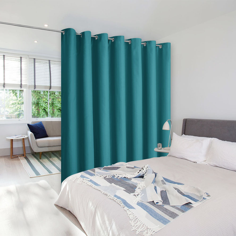 Teal grommet top room divider curtain separating a bed from a small living area in a bright, modern room.