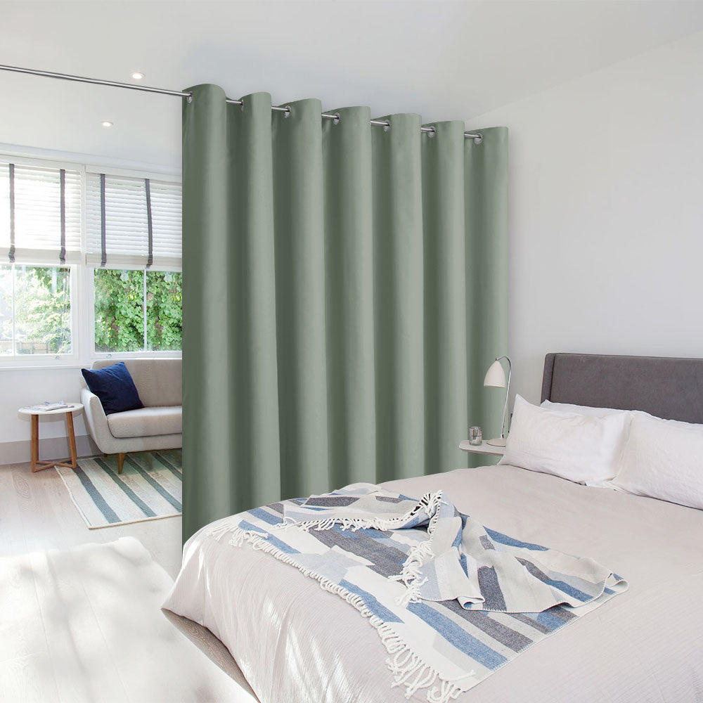 Sage green room divider curtain on a tension rod separating a bedroom from a living area in a bright, modern studio space.