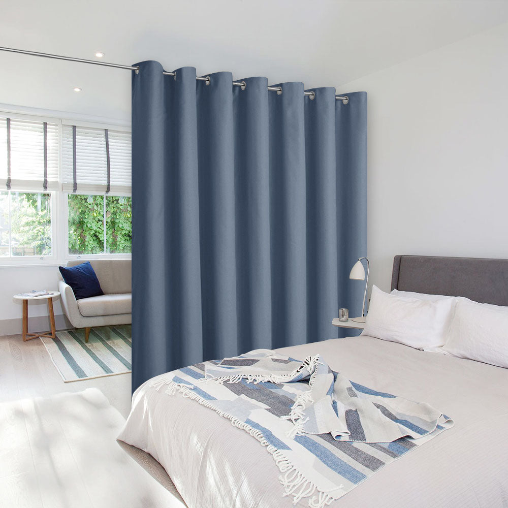 A slate blue room divider curtain separating a bedroom area from a sunlit living space in a studio.