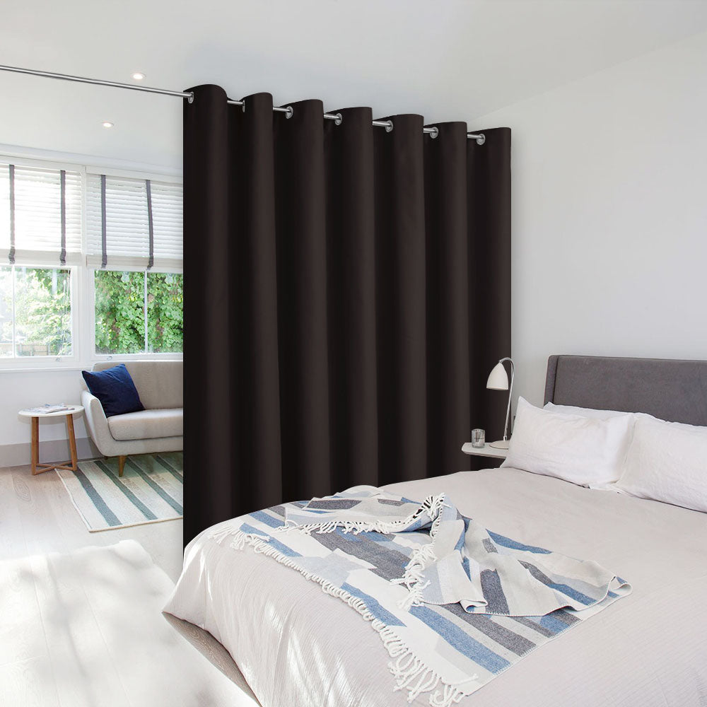 A thick black room divider curtain hung on a rod to separate a bedroom from a sunlit living room area.