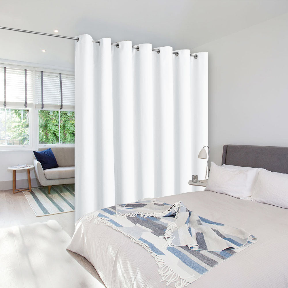 White room divider curtain with grommets hung from a ceiling rod to separate a bedroom from a sunlit living area.