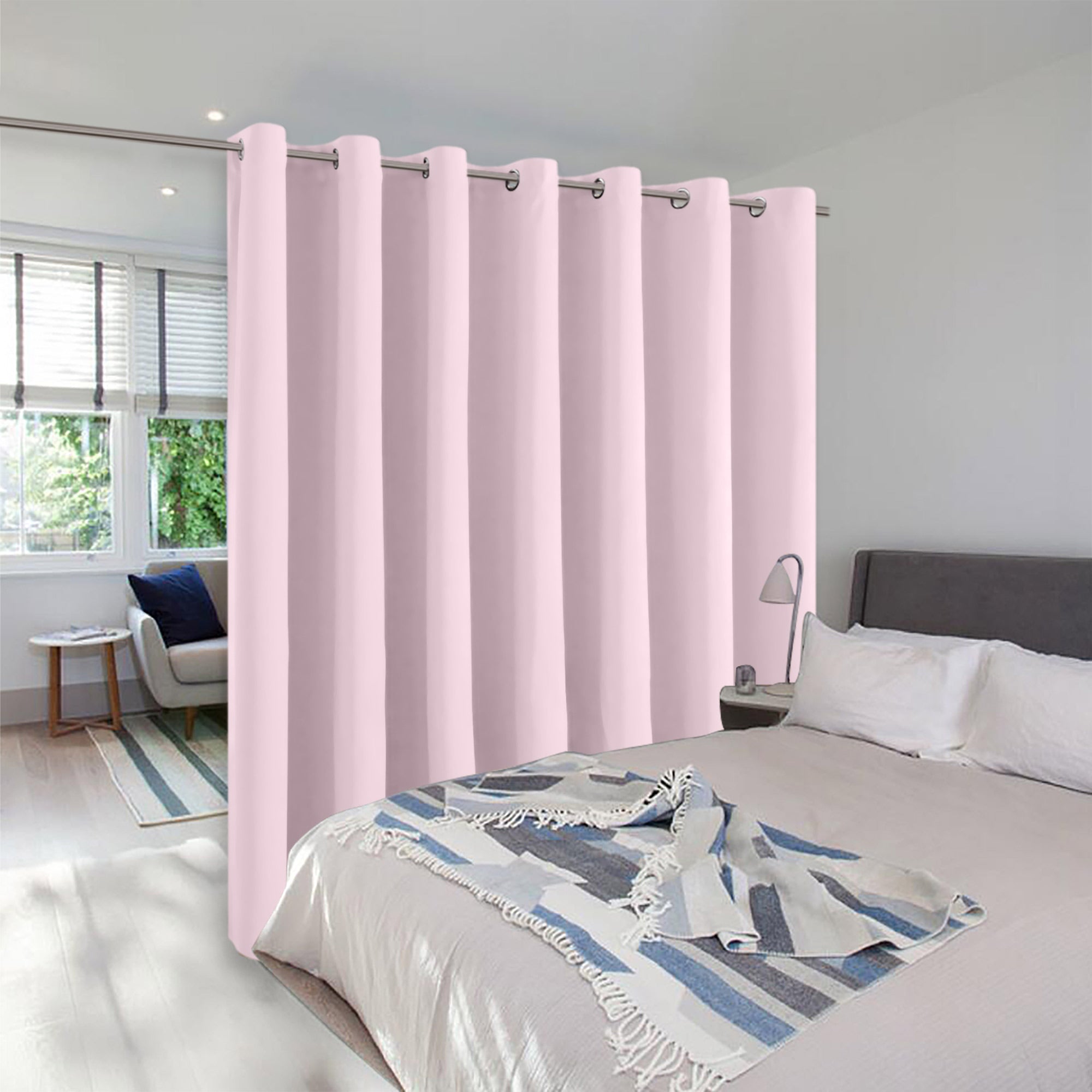 A light pink grommet-top room divider curtain separates a bedroom from a sitting area, creating two distinct living spaces.
