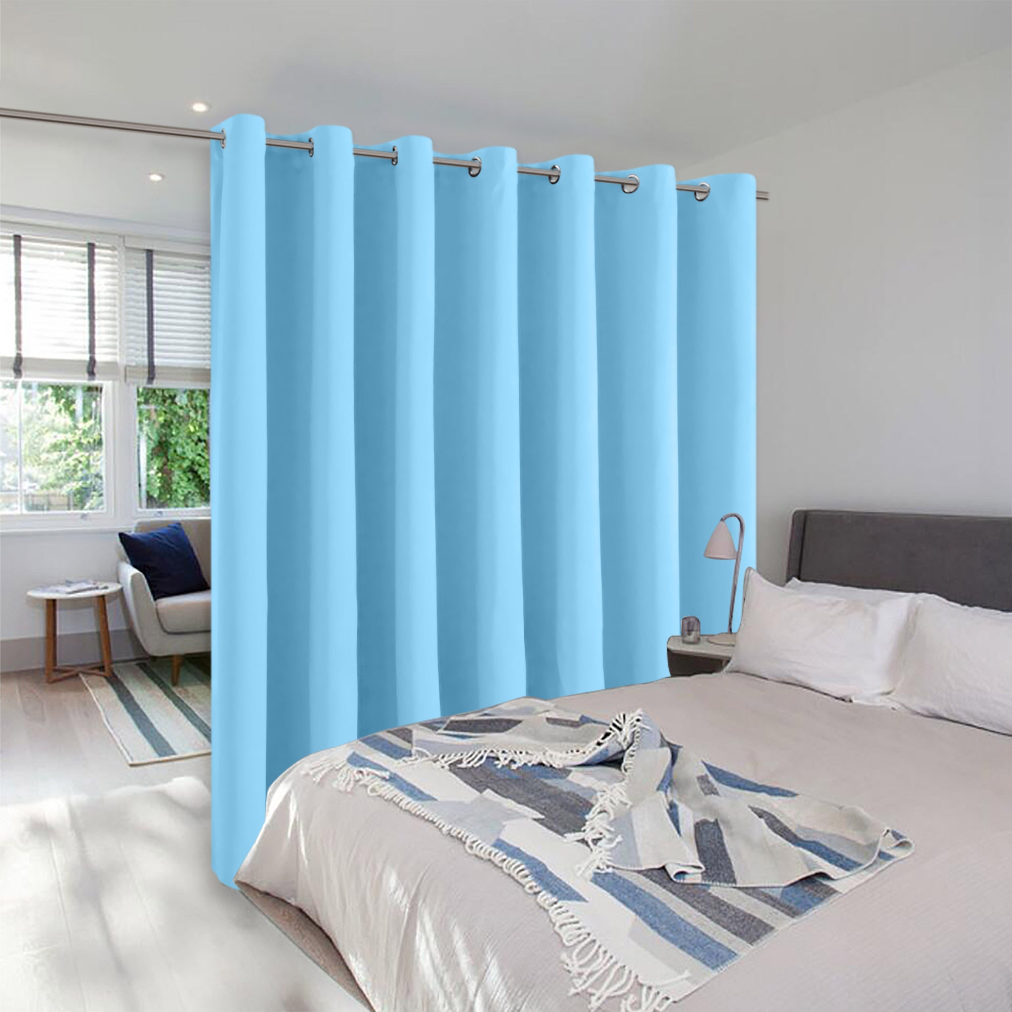 Light blue grommet top room divider curtain creating privacy between a bed and a sitting area in a bright room.