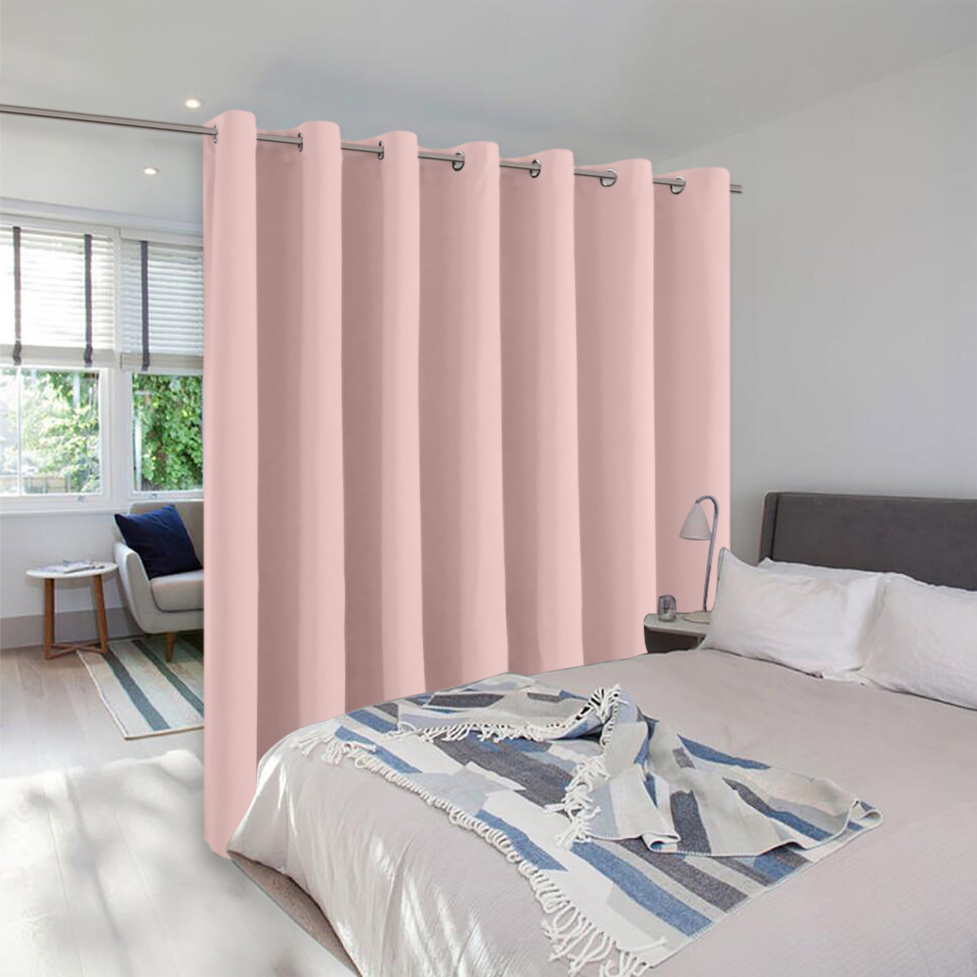 A light pink grommet room divider curtain creating privacy between a bed and a small, sunlit sitting area.