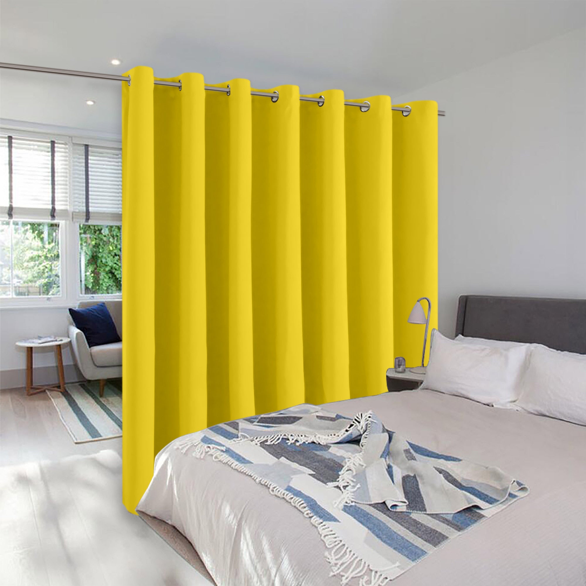 A bright yellow grommet curtain used as a room divider, separating a bedroom from a sunlit sitting area.