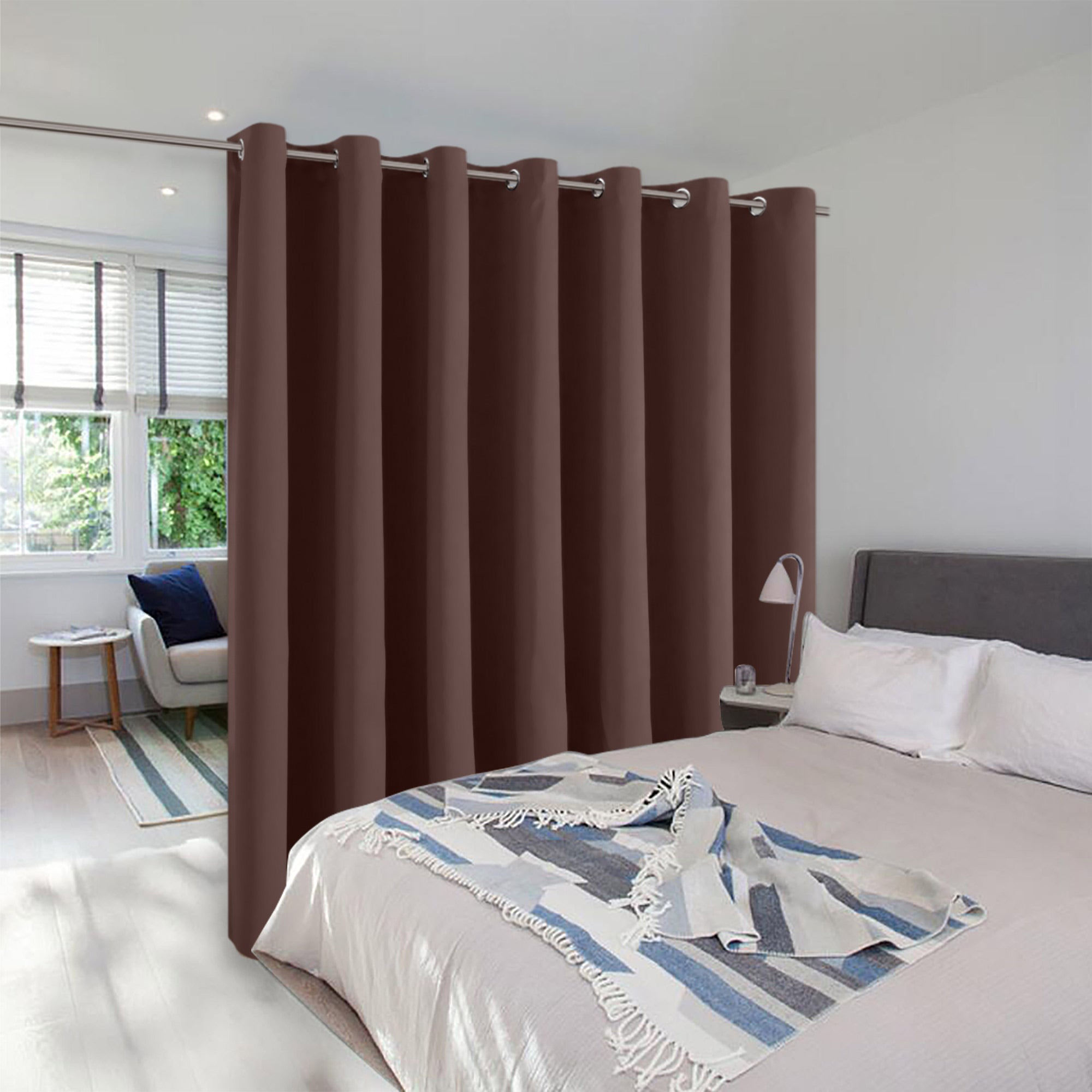 A brown grommet top room divider curtain creates privacy, separating a bedroom from a sunlit seating area.