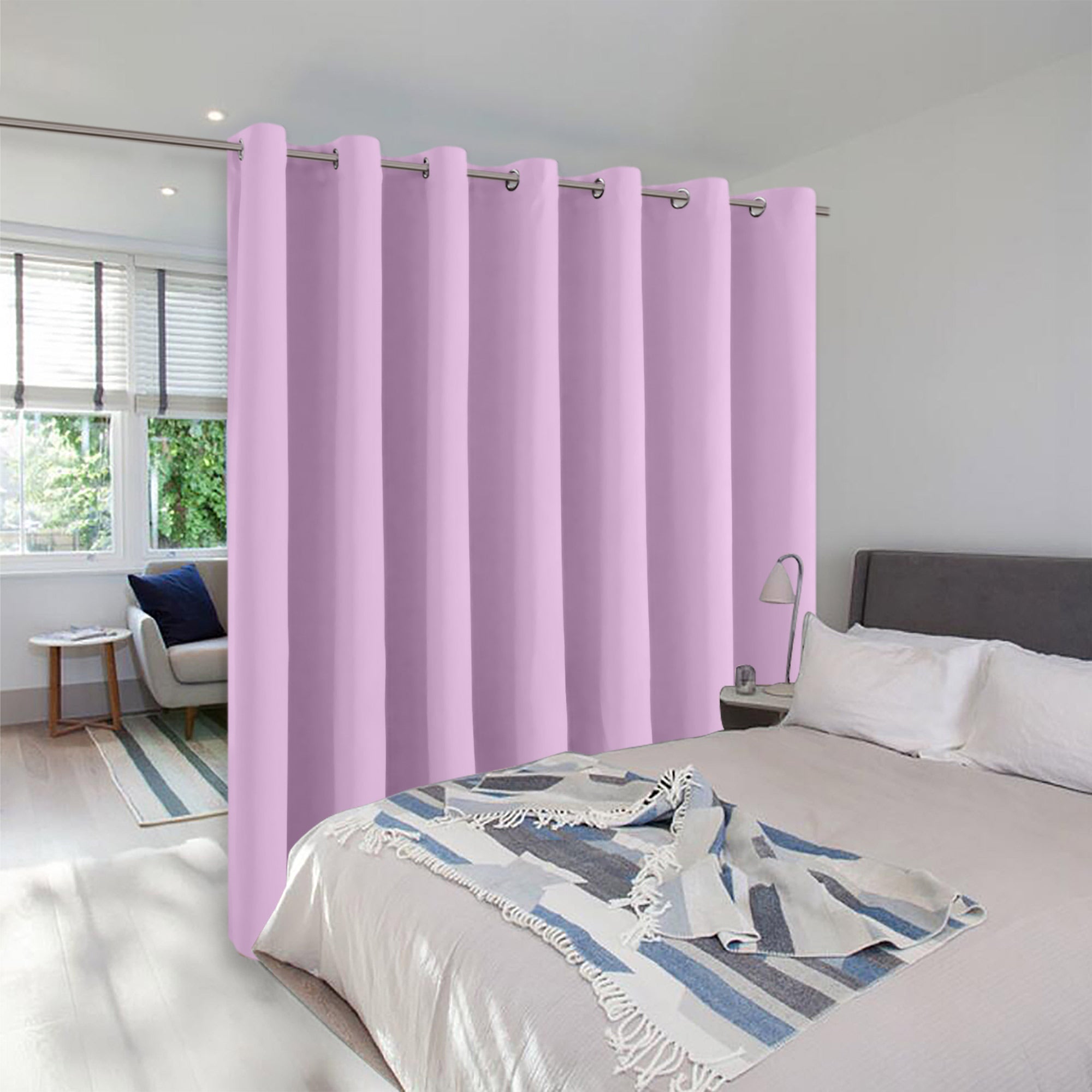 A light purple grommet top room divider curtain creates privacy, separating a bed from a sunlit sitting area.
