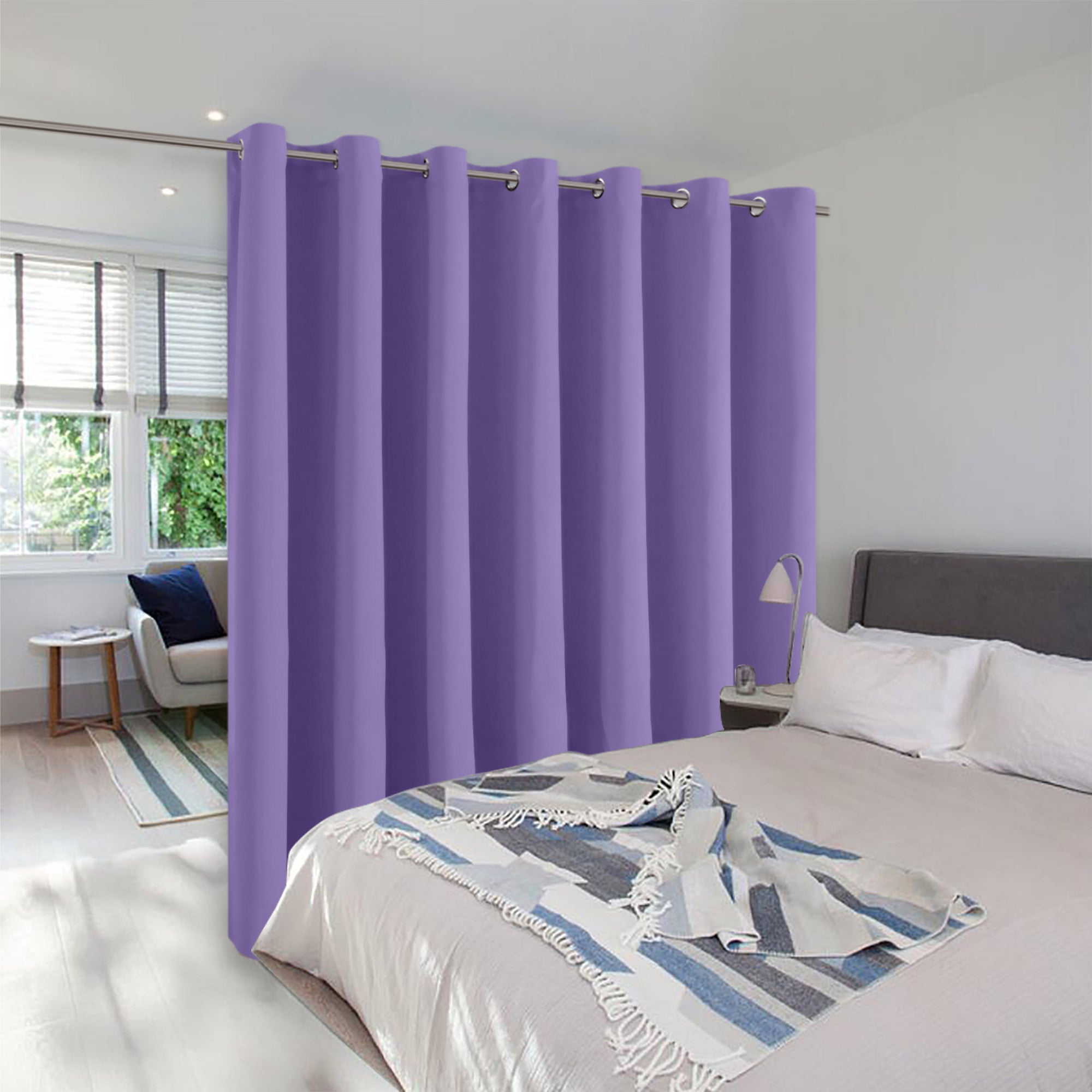 A purple grommet-top room divider curtain creates privacy, separating a bed from a sunlit sitting area in a modern bedroom.