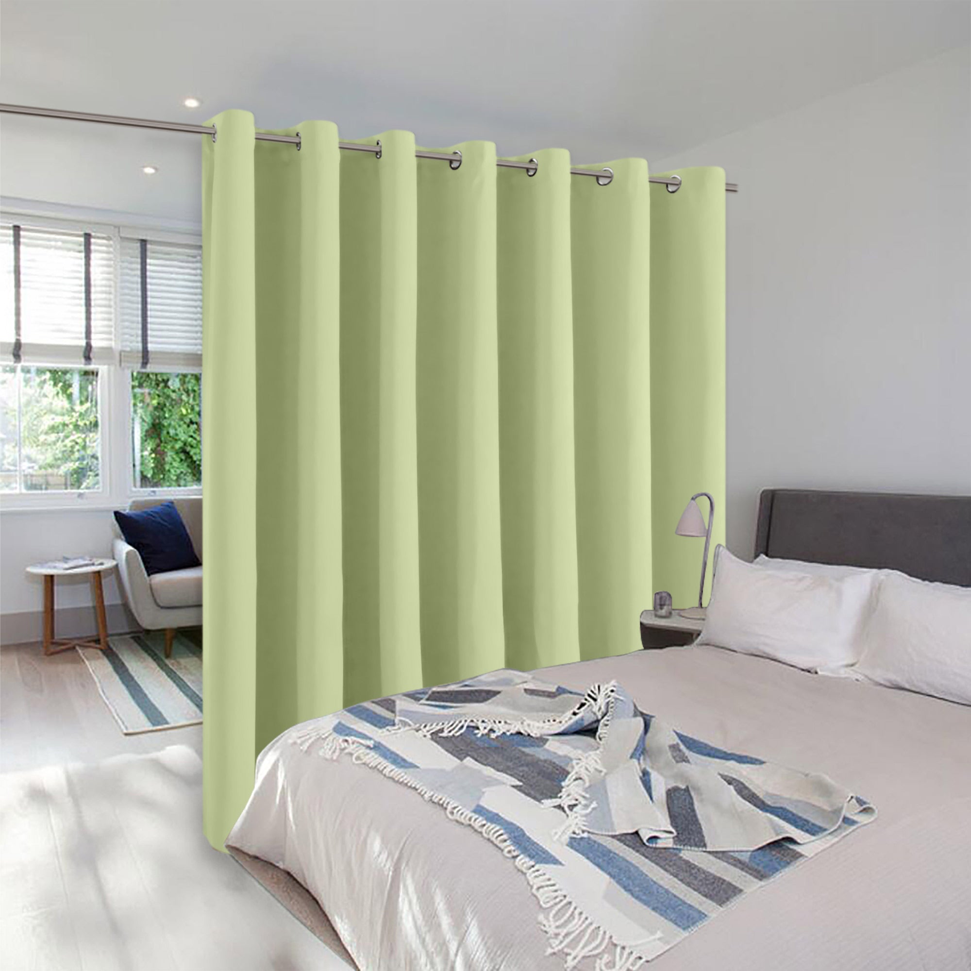 Light green room divider curtain with silver grommets separating a bedroom sleeping area from a small living space.
