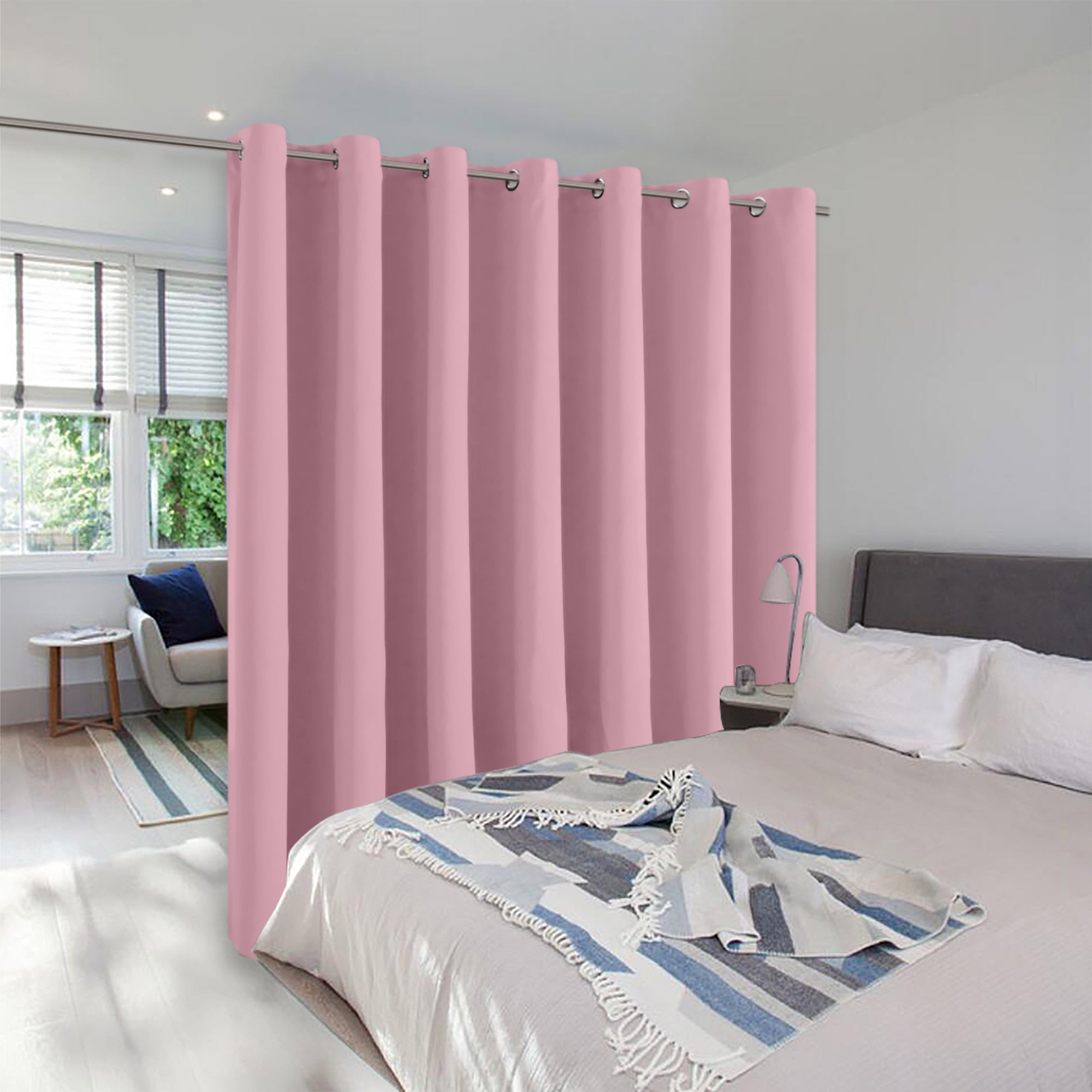A pink grommet room divider curtain creating a private partition between a bed and a sitting area in a modern room.