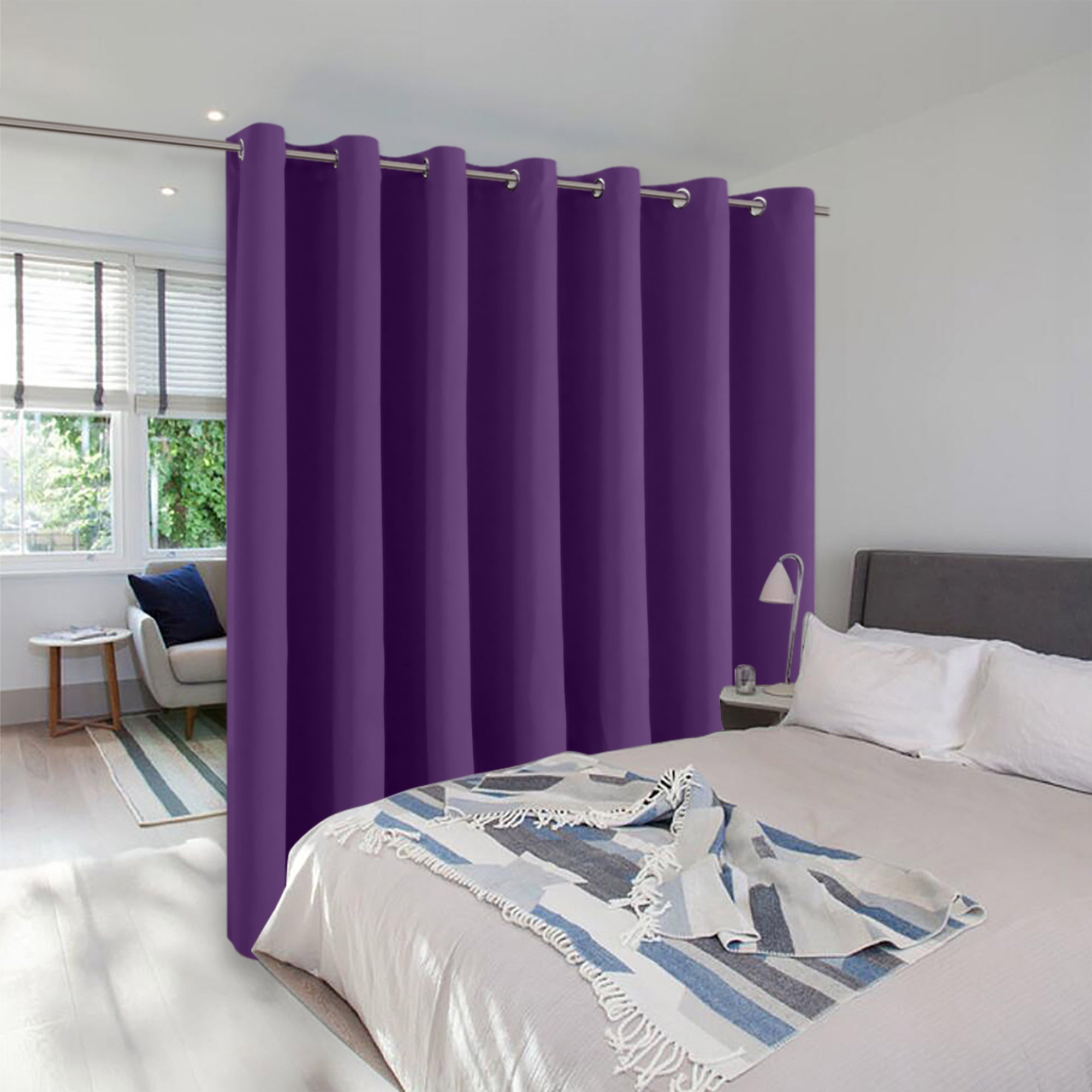 A long purple room divider curtain with silver grommets creates a privacy partition between a bed and a sitting area.