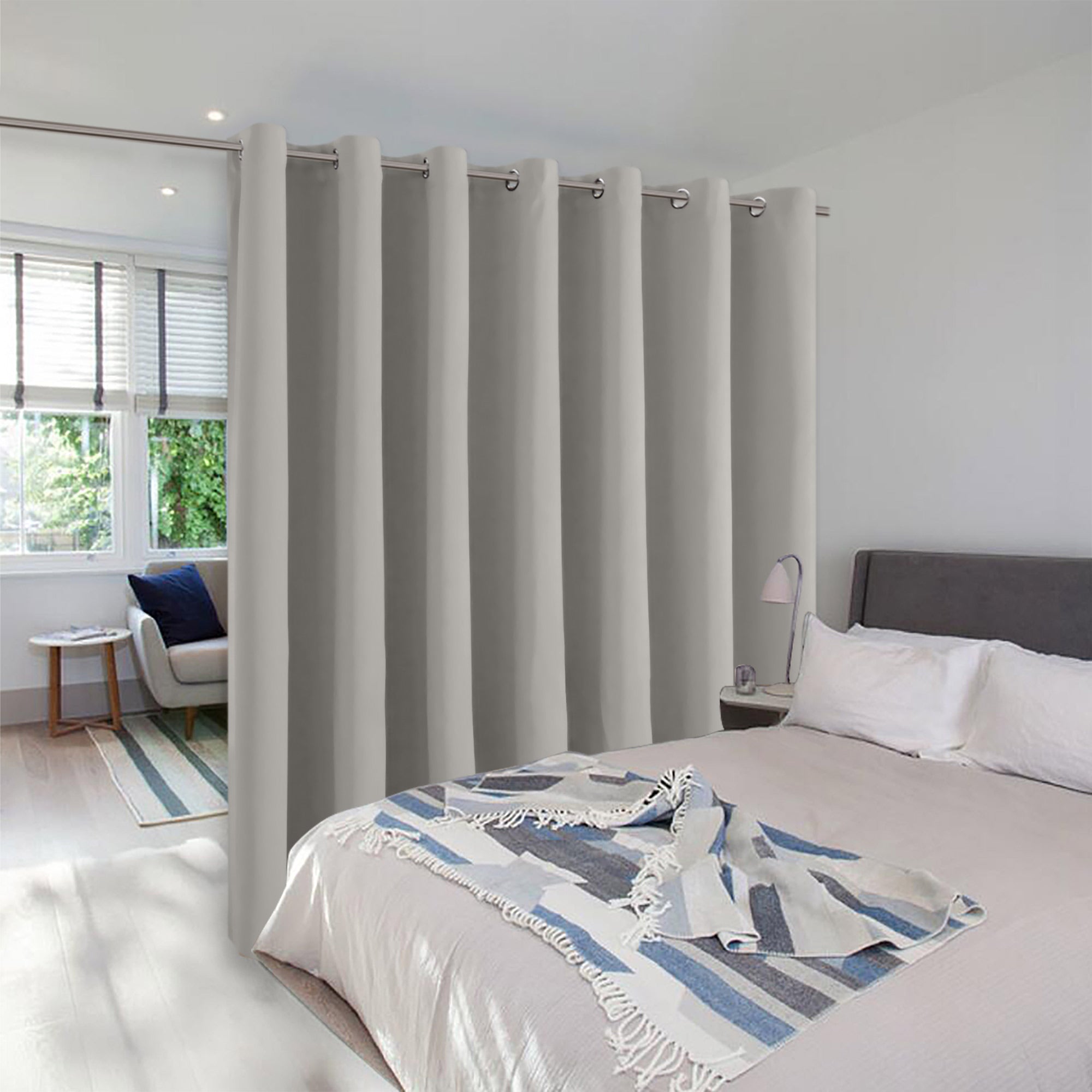Light gray grommet room divider curtain creating a private sleeping area in a modern bedroom with a separate sitting nook.