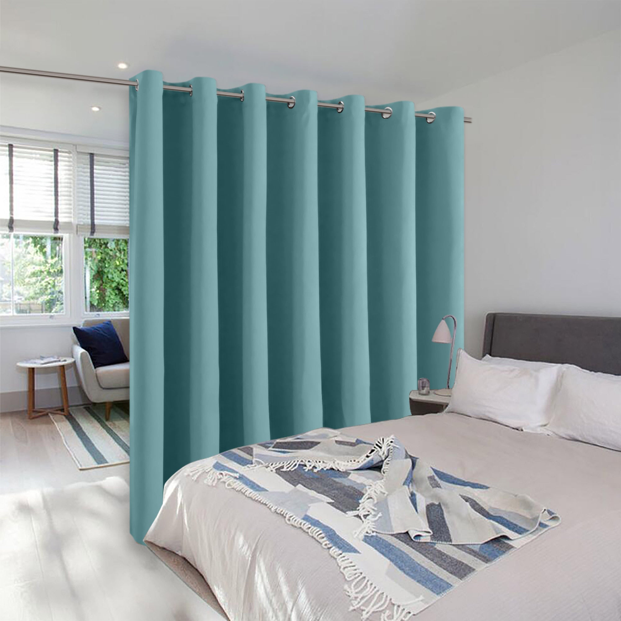 A teal room divider curtain with silver grommets hangs in a bedroom, creating a separate sitting area by a window.