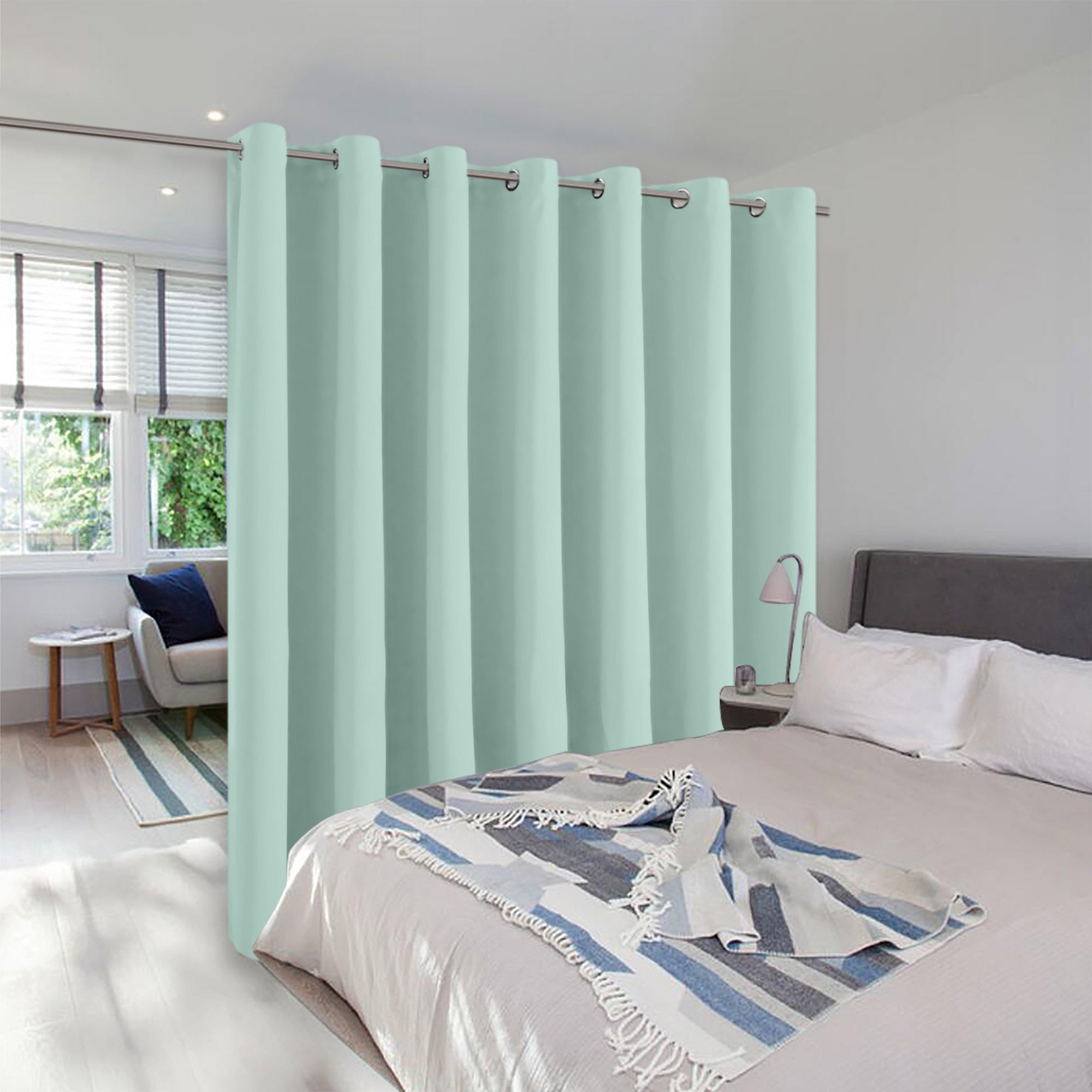 Light green room divider curtain with grommets separating a bedroom space from a small, bright sitting area by a window.