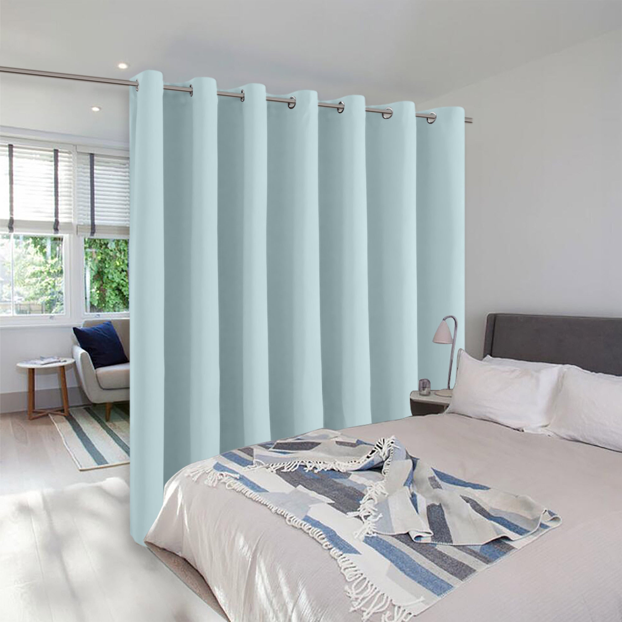 Light blue room divider curtain with silver grommets hangs in a bedroom, creating a separate private nook by the window.