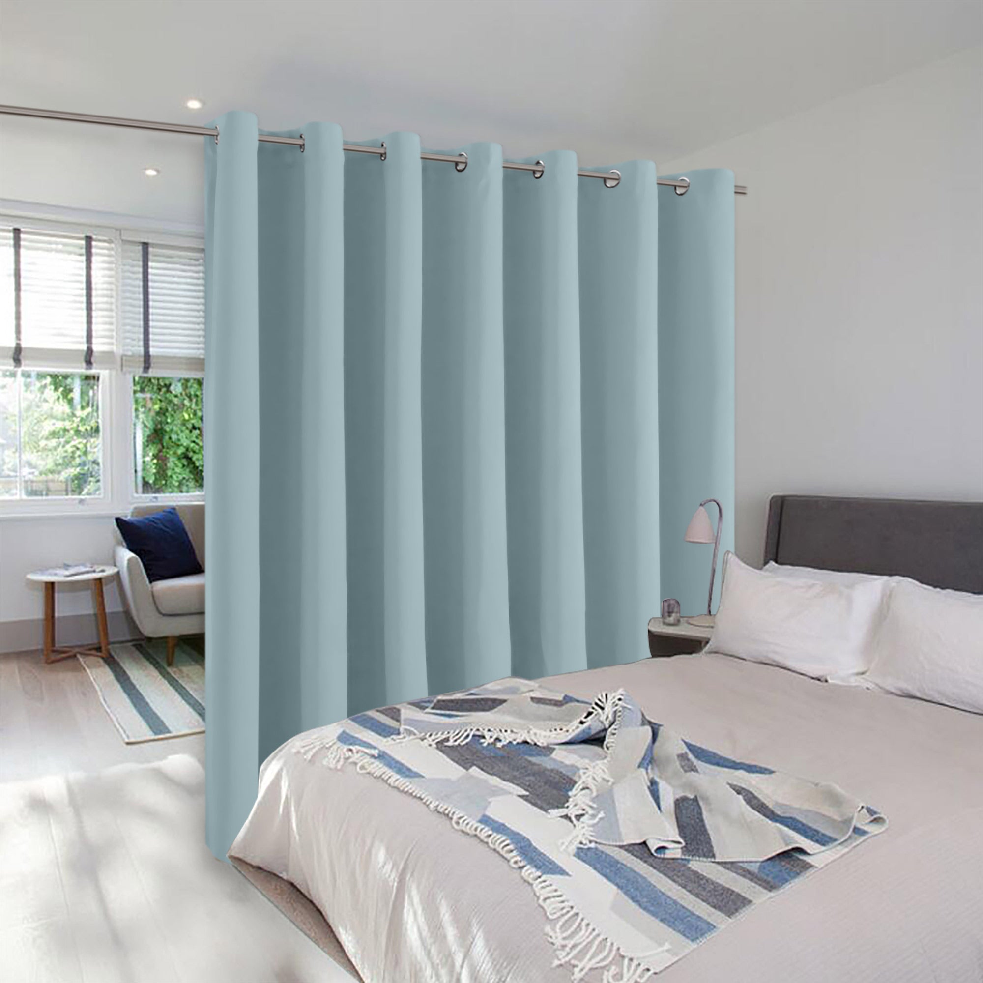A light blue grommet curtain on a ceiling track divides a modern bedroom, creating a separate seating area by a window.