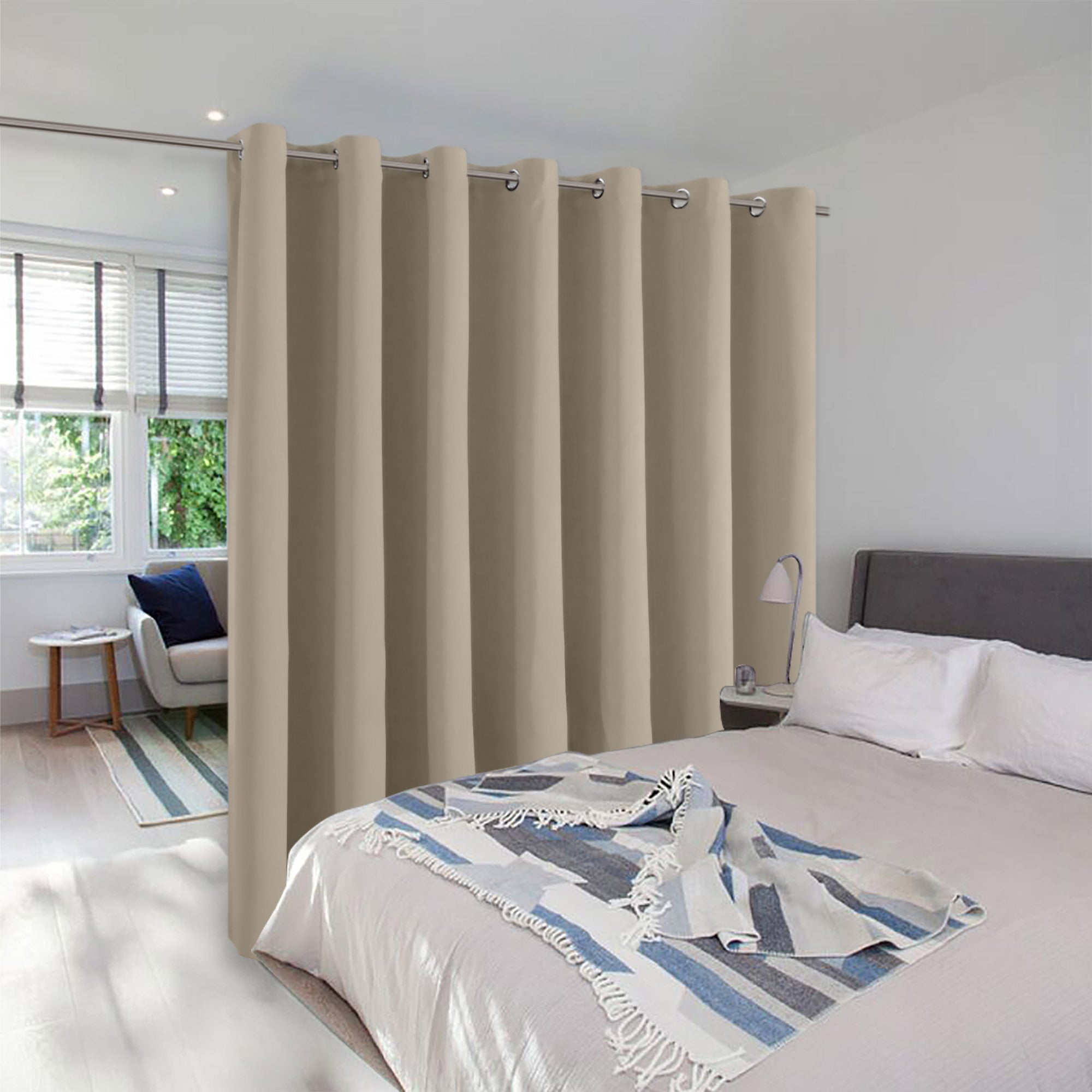 Beige room divider curtain with silver grommets separating a bedroom sleeping area from a small living space.