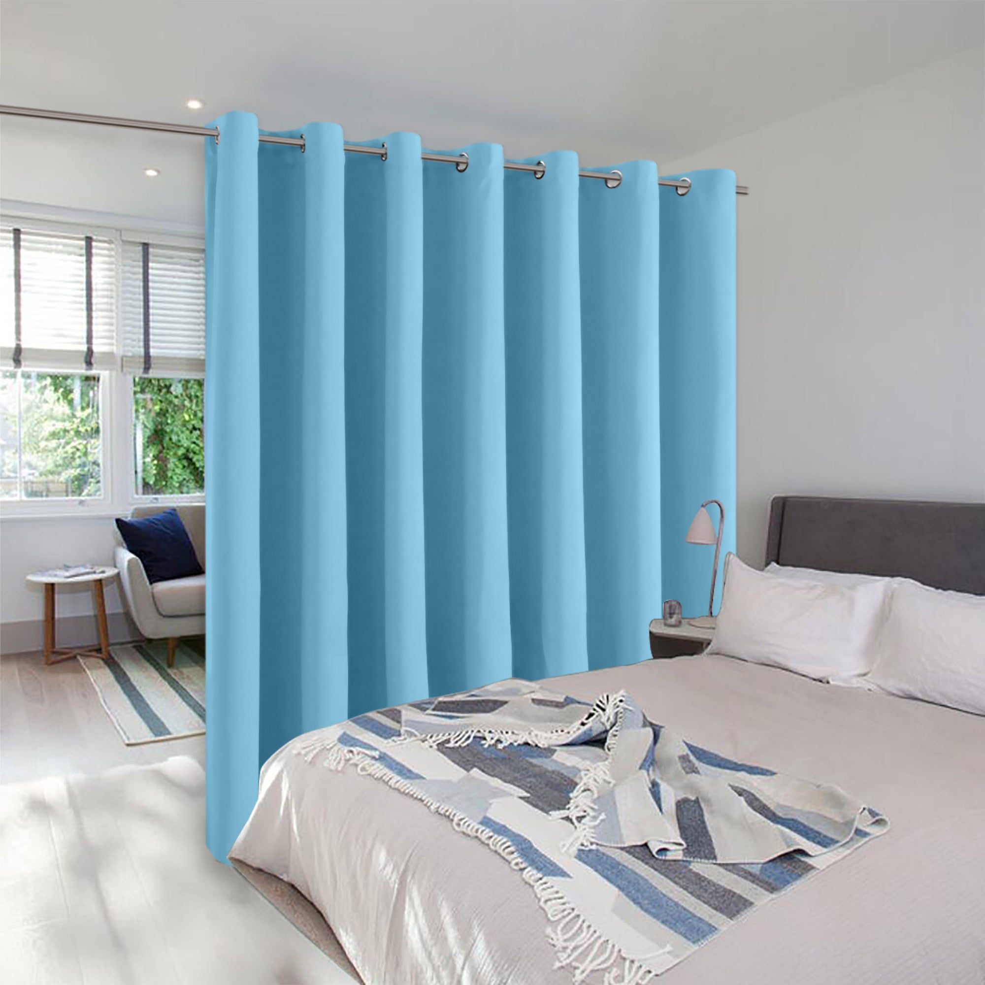 A light blue room divider curtain with metal grommets separating a bed from a seating area to create a private space.