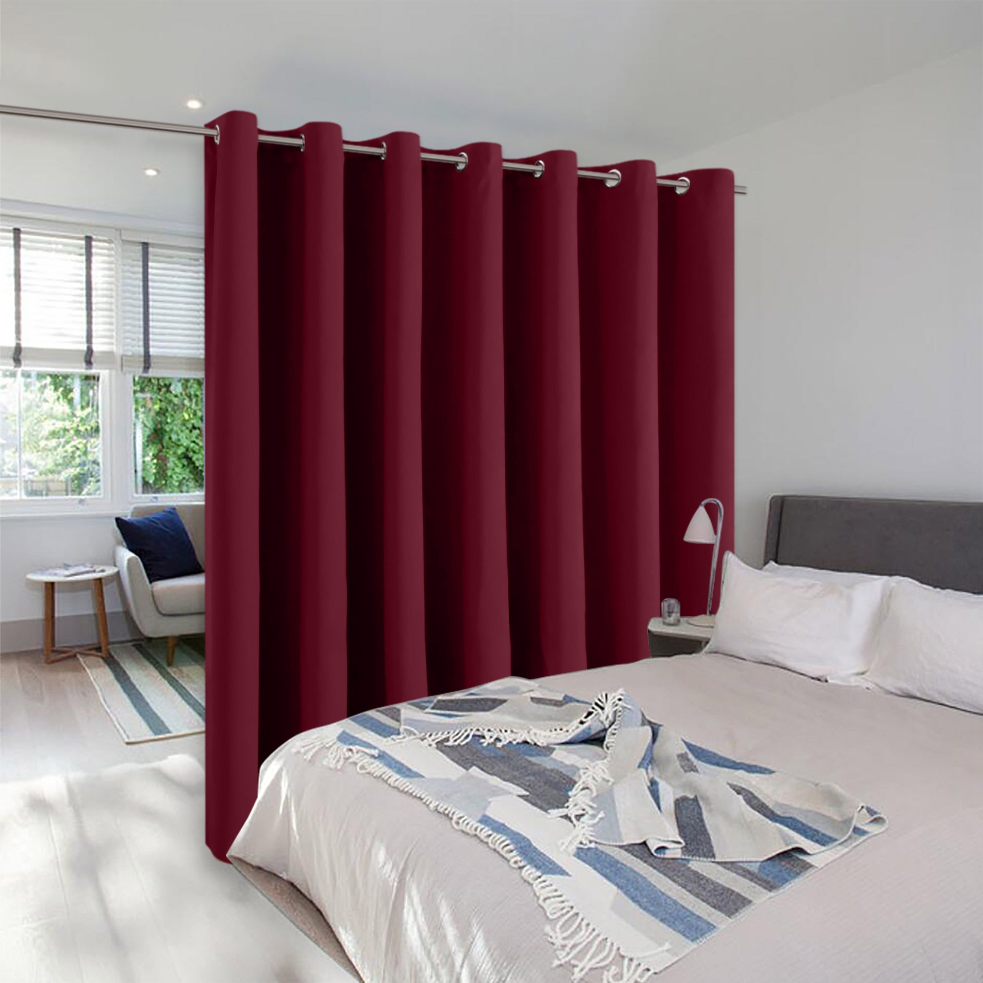 Burgundy room divider curtains with silver grommets creating a partition between a bed and a bright sitting area.