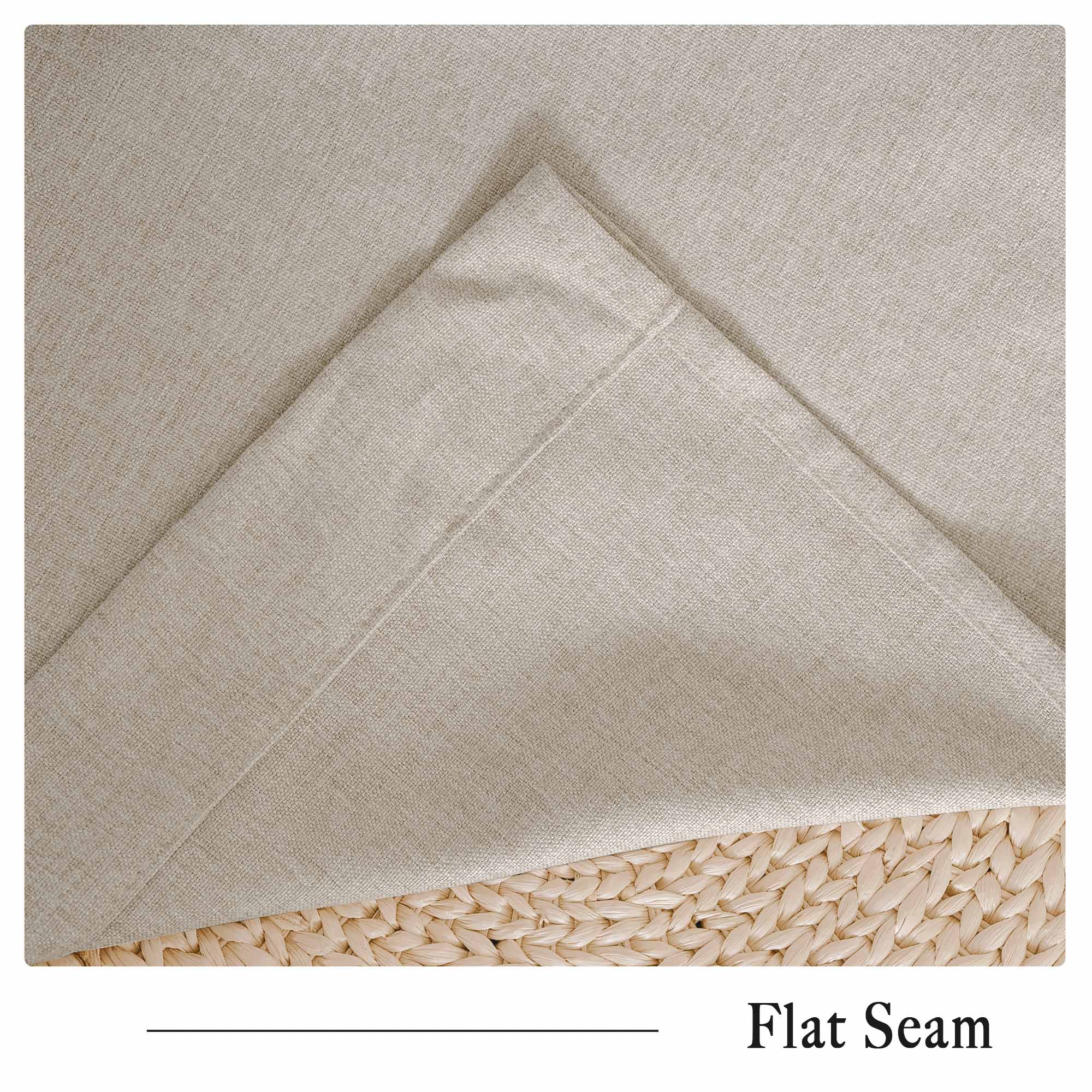 Soft beige cotton linen curtain fabric detail, highlighting the natural textured weave and flat seam, resting on a woven surface.