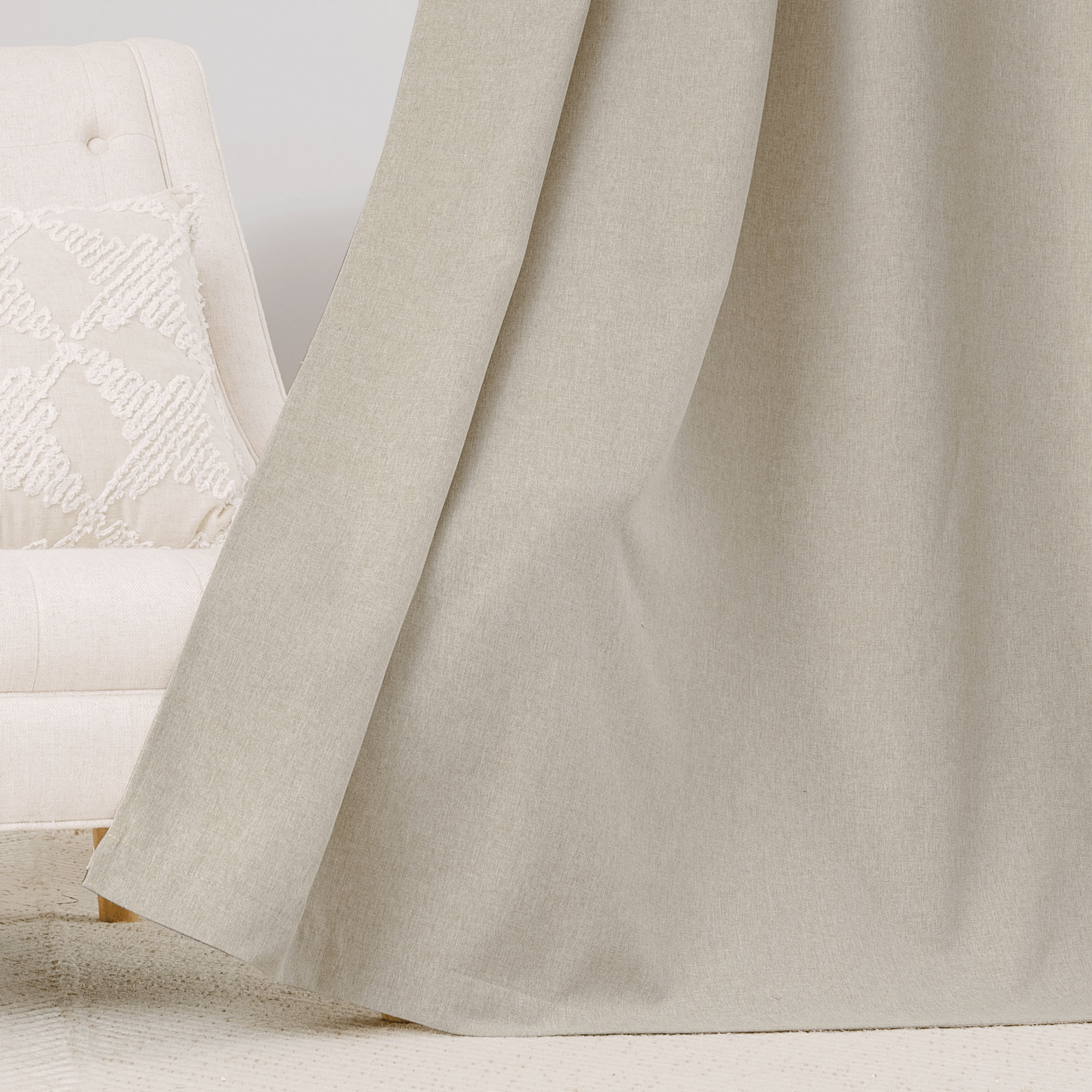 Close-up of a light beige soft cotton linen curtain fabric, showing its natural texture and gentle drape next to an armchair.
