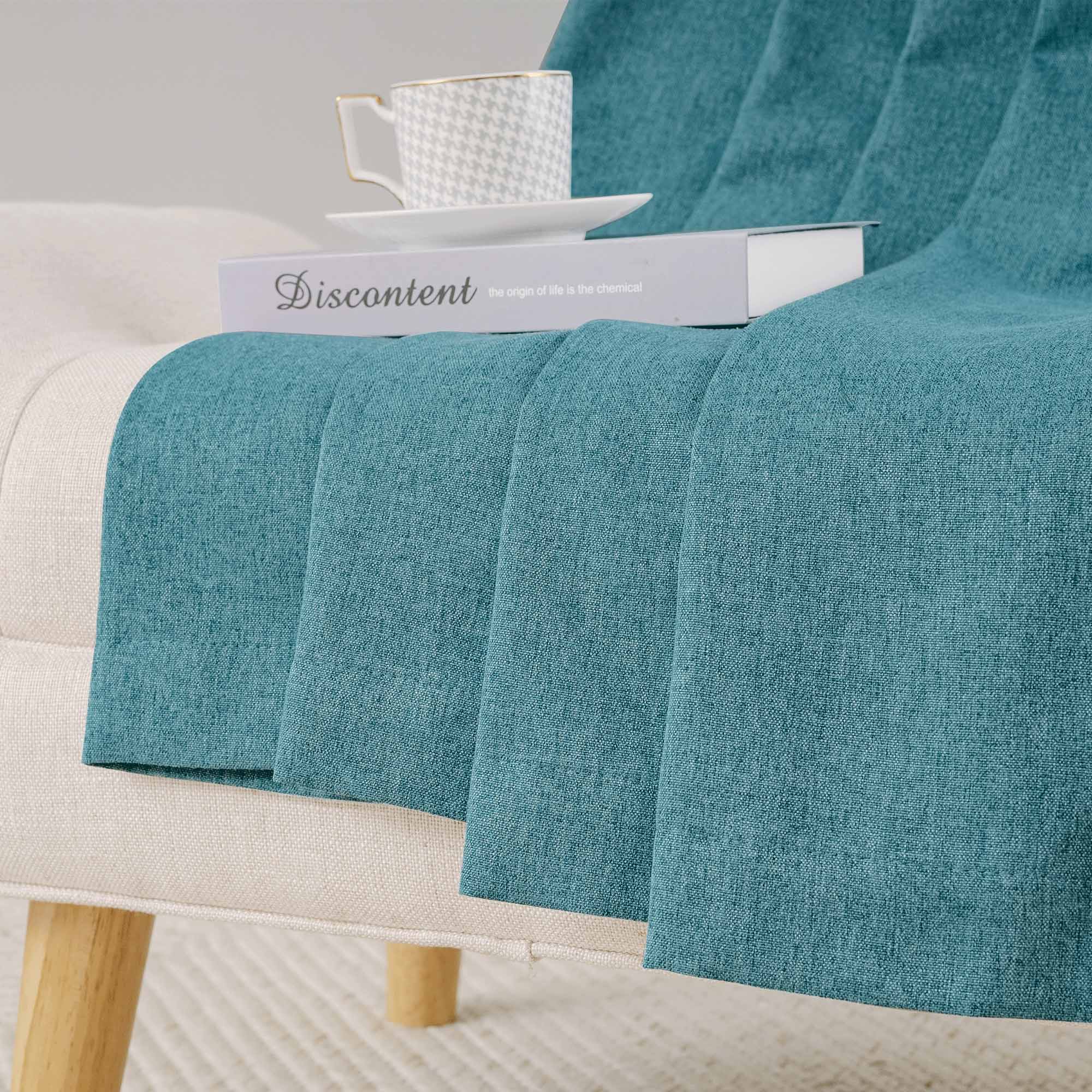 Close-up of soft teal blue cotton linen curtain fabric draped over an armchair, showing its textured weave and elegant folds.