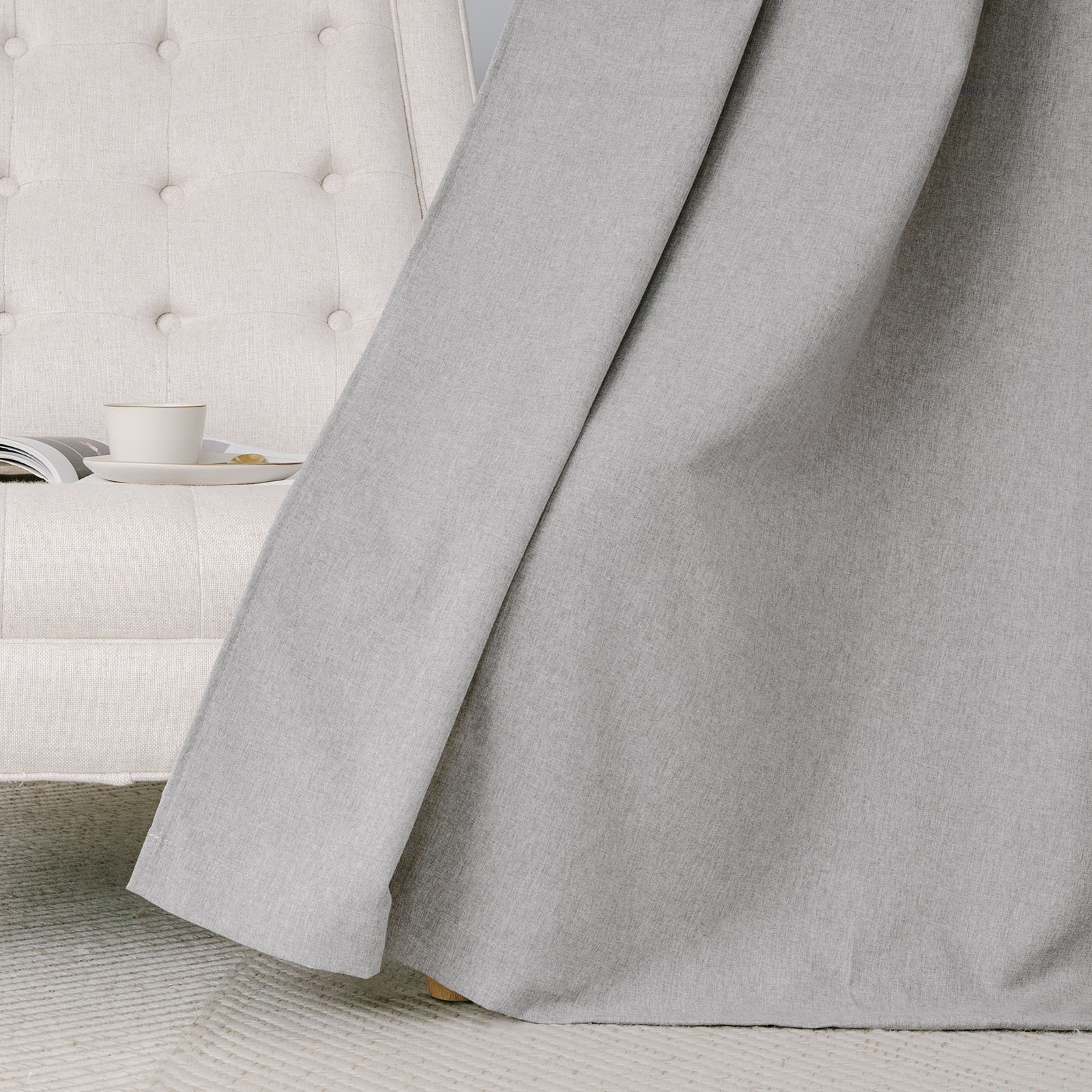 Soft grey cotton linen curtain fabric draped next to a tufted armchair, highlighting its natural texture and smooth fall.