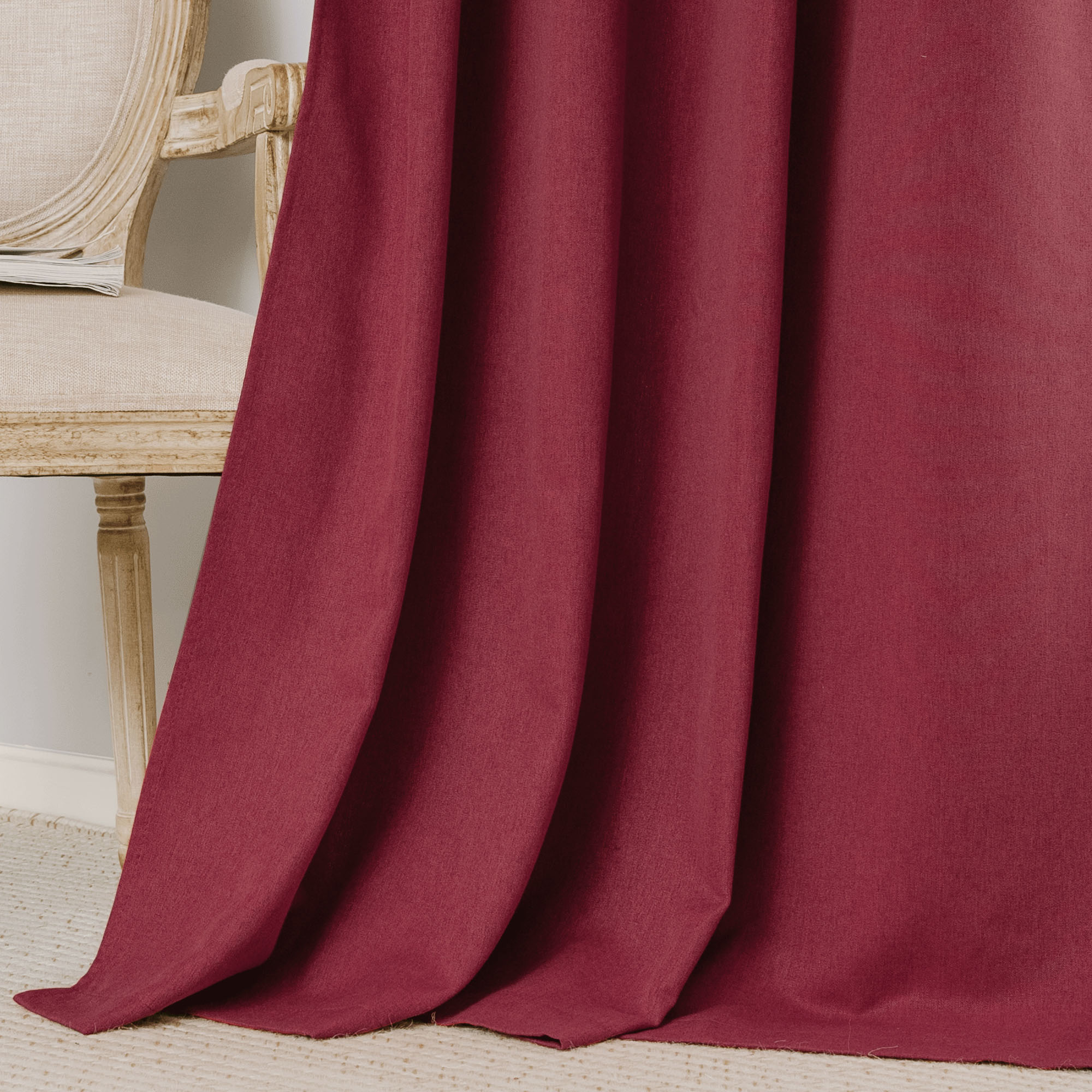 Soft maroon cotton linen curtain draped, showcasing the rich fabric texture and natural folds. Part of a light beige chair is visible.