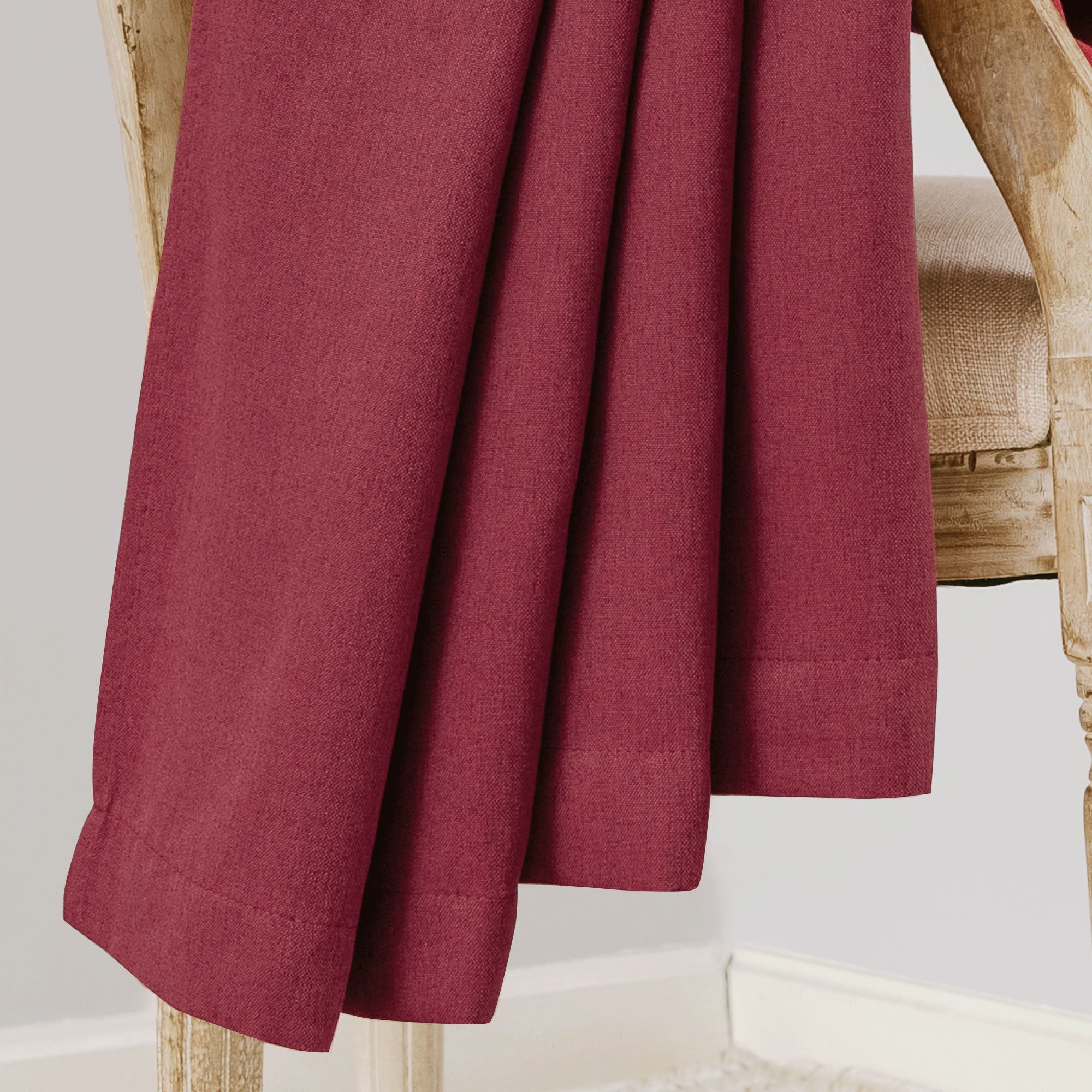 Close-up of deep red soft cotton linen curtain fabric, highlighting its woven texture and smooth drape over a wooden chair.