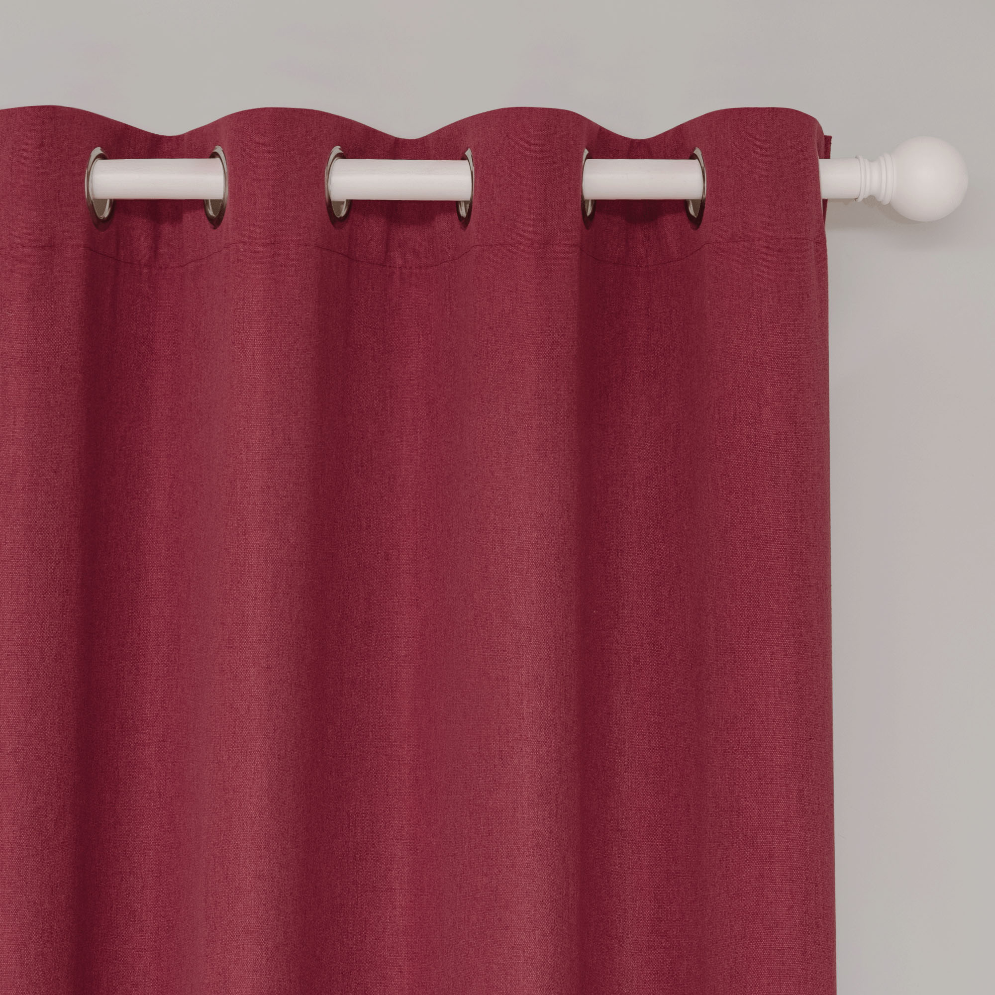 Close-up of a deep red soft cotton linen curtain with silver grommets on a white rod, showcasing the fabric texture.