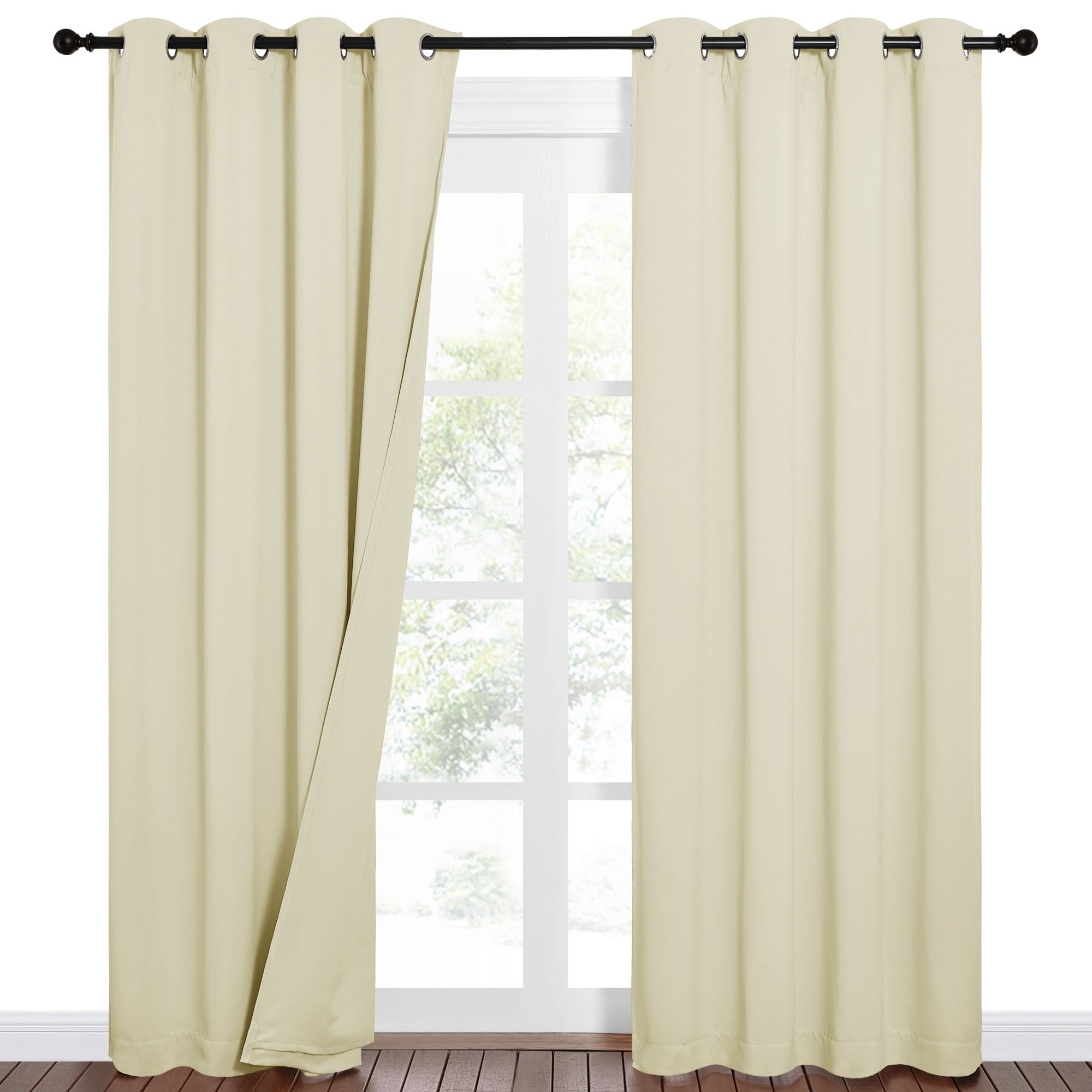 Off-white Sound Barrier blackout curtains with grommets hanging on a rod before a window, with one panel pulled aside.
