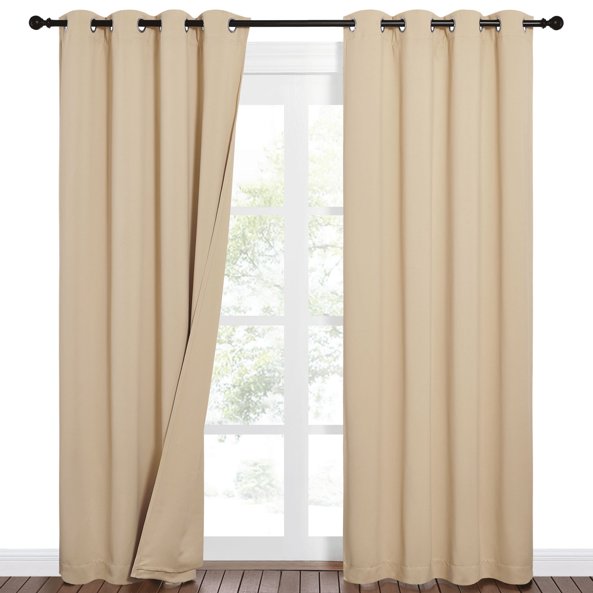 Tan Sound Barrier 100% blackout grommet curtains on a dark rod, one panel open to reveal a bright window view and wood floor.
