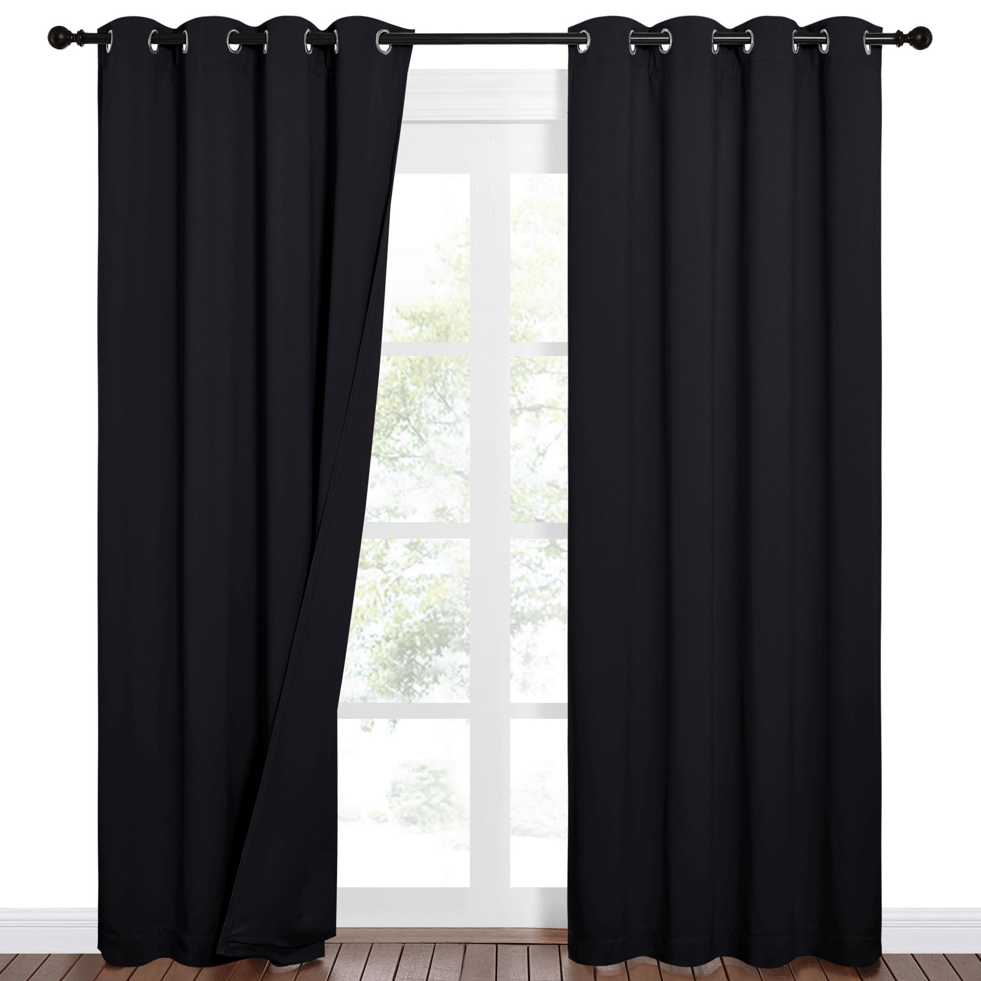 Pair of black Sound Barrier 100% blackout curtains with silver grommets, one curtain slightly open revealing a bright window.