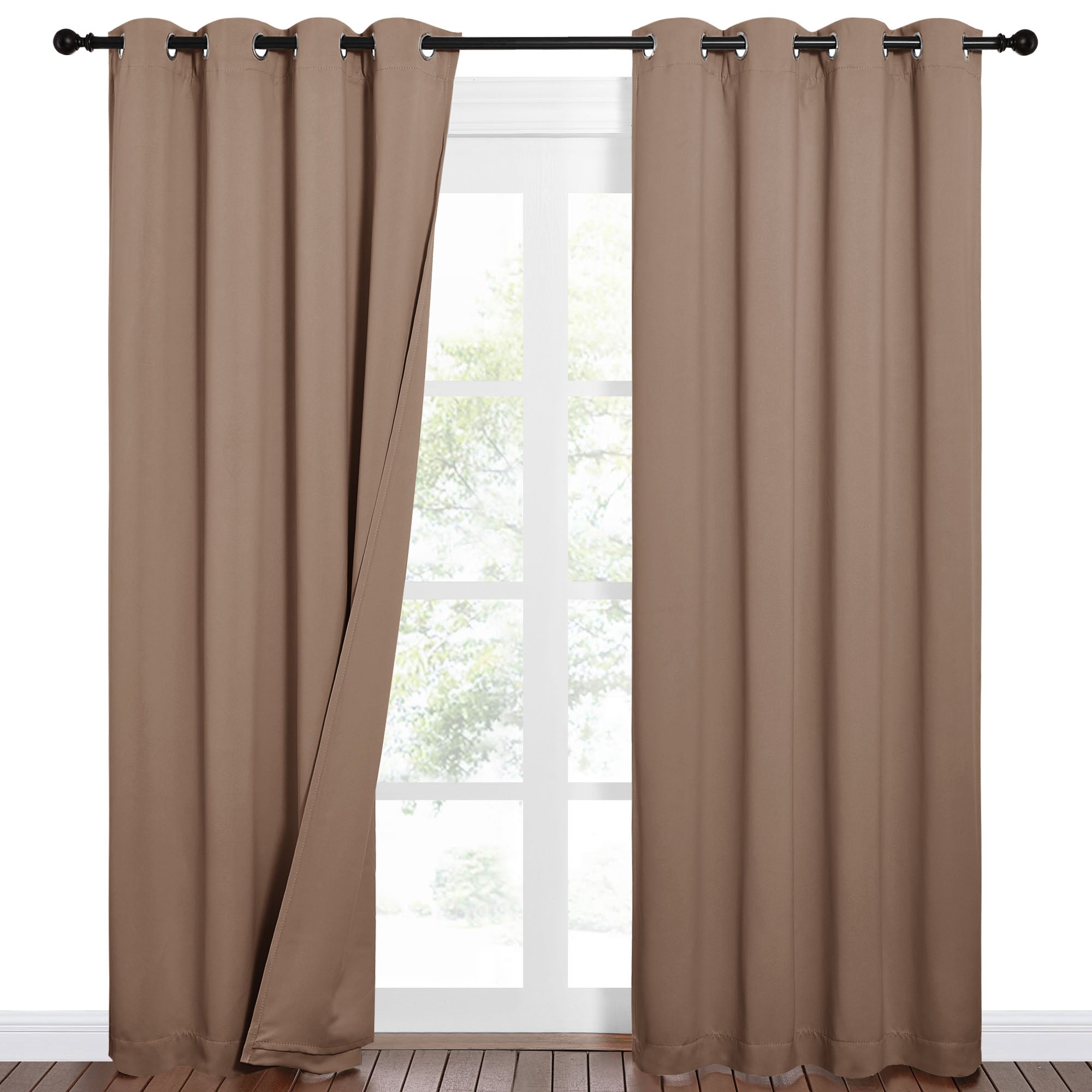 Brown grommet top blackout curtains, one panel slightly open, hangs on a black rod over a window with a view of trees.