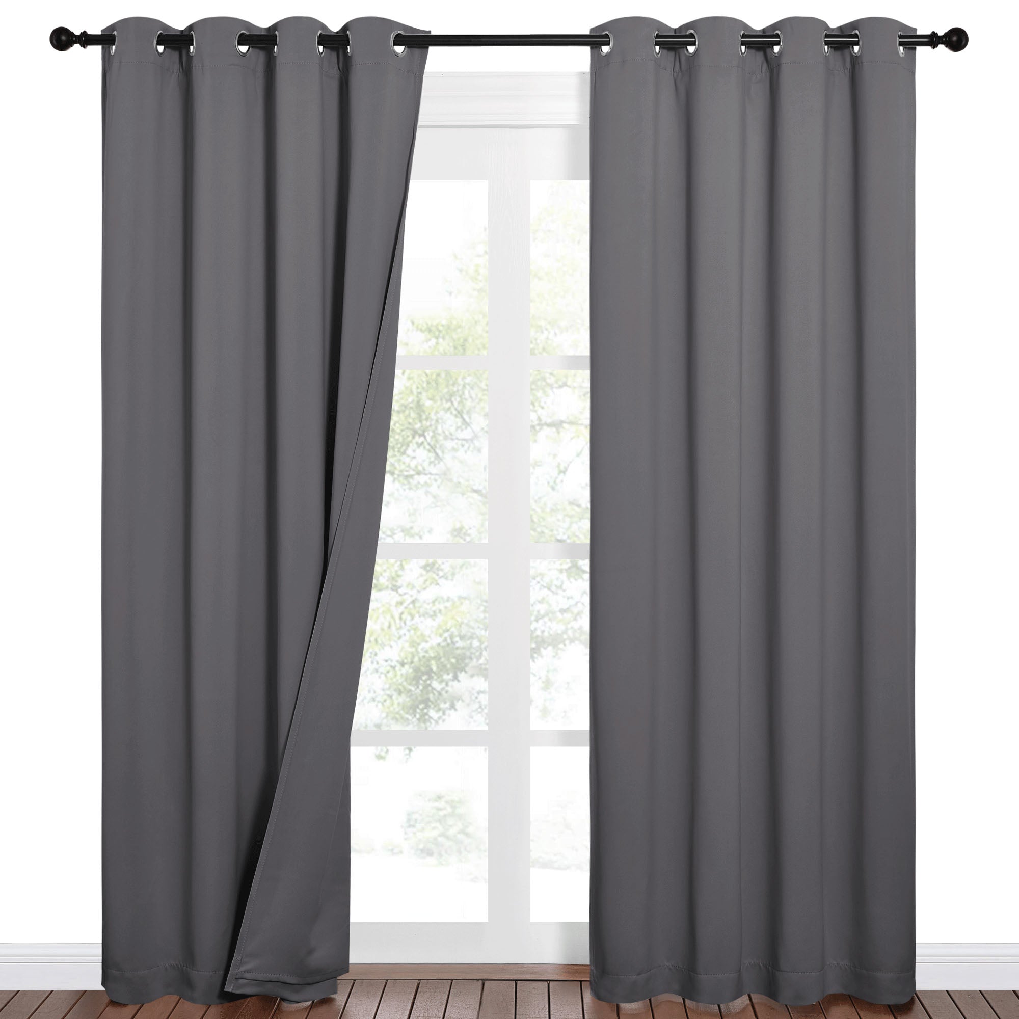 A pair of dark grey Sound Barrier 100% blackout curtains with silver grommets hanging on a black rod in front of a window.