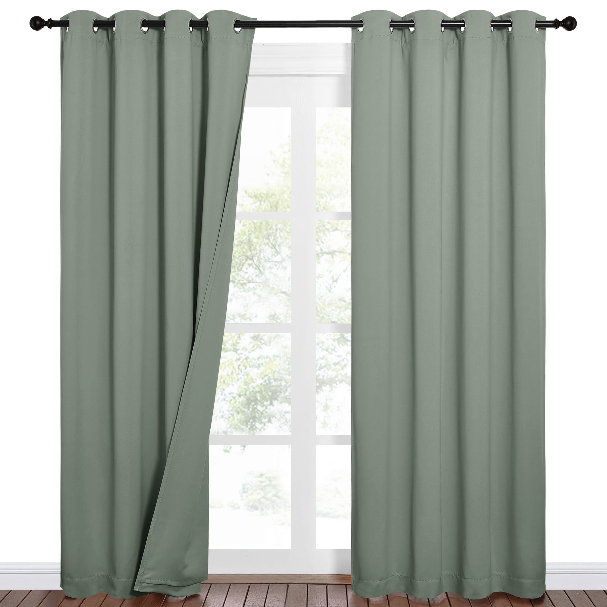 Sage green 100% blackout curtains hanging on a dark rod, one panel slightly open to reveal a window. Perfect for privacy & light control.