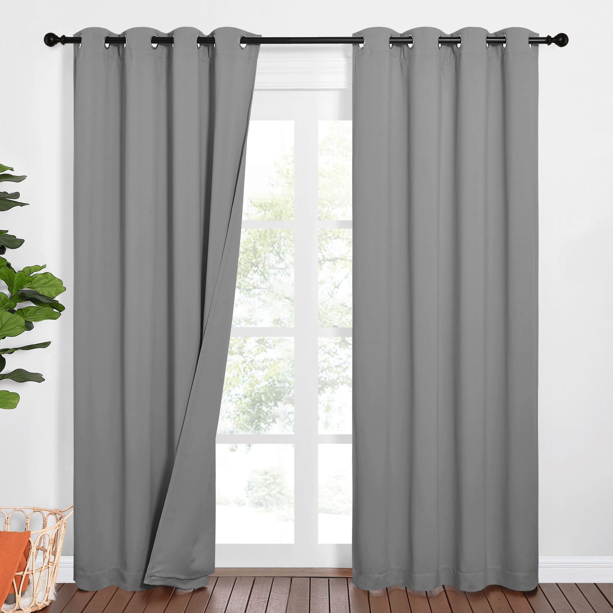 Pair of grey Sound Barrier 100% blackout curtains with grommets on a black rod; one slightly open revealing a window.