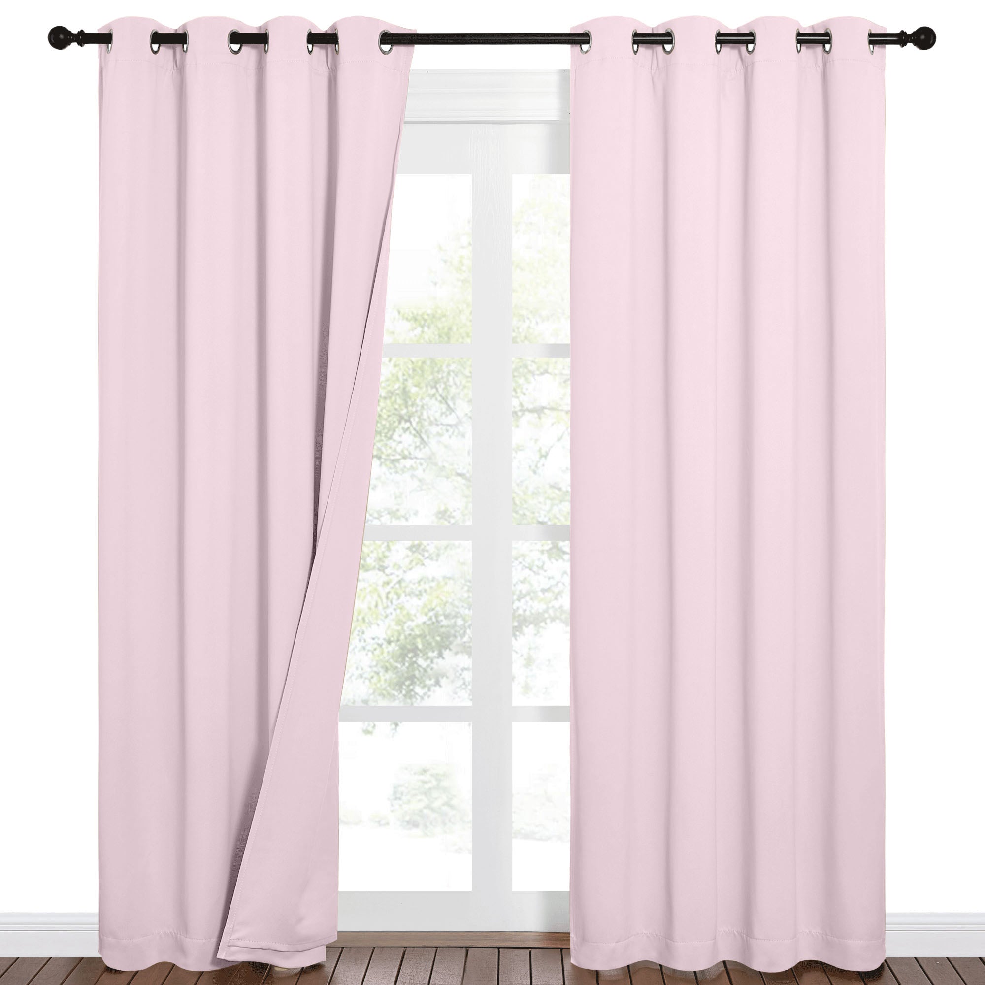 Light pink 100% blackout grommet curtains on a black rod, one panel slightly open, revealing a window view.