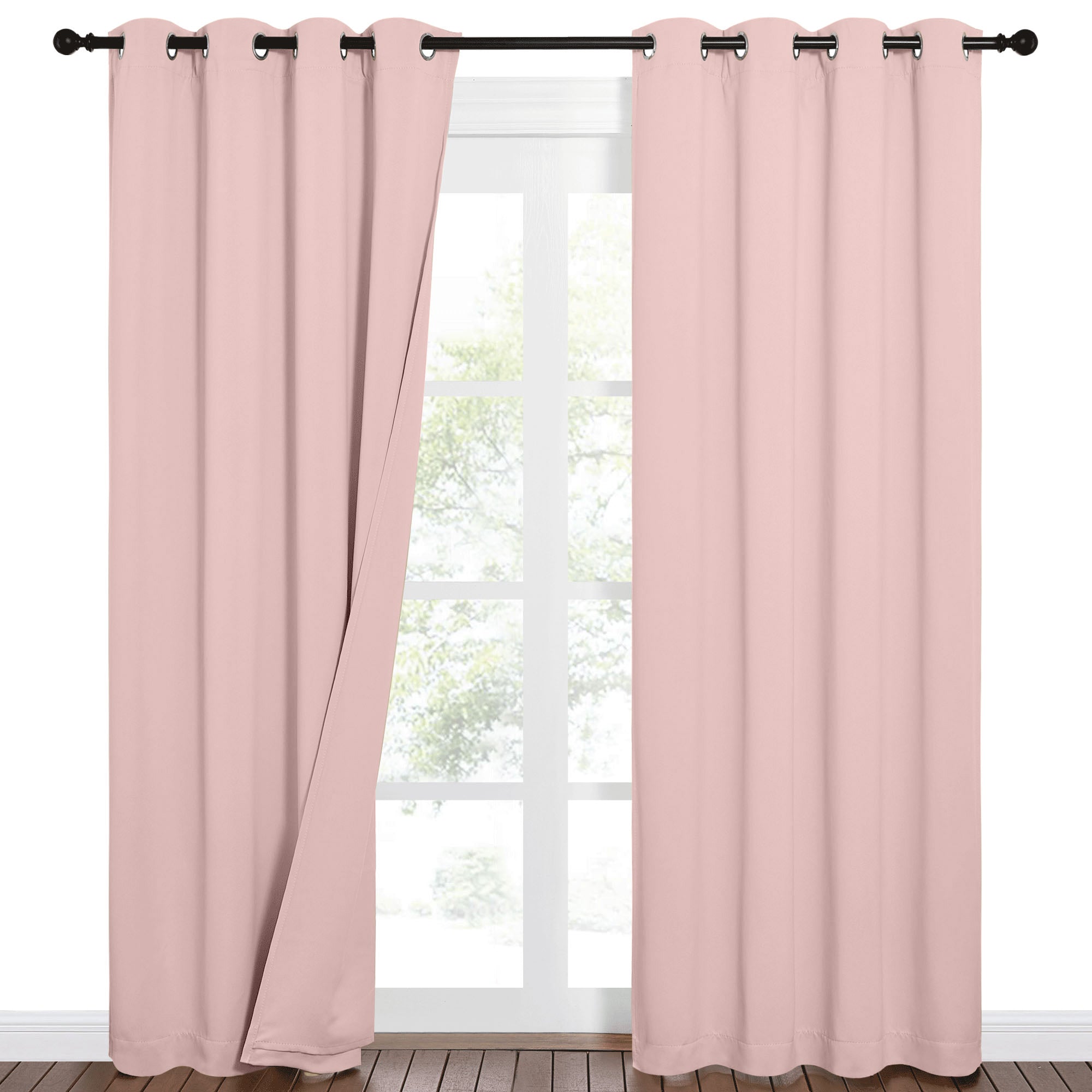 Blush pink 100% blackout grommet top curtains on a black rod, one panel partially open against a window.