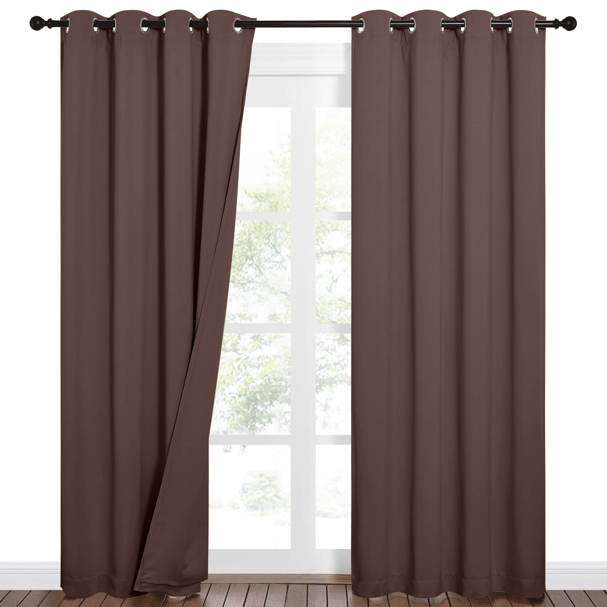 Brown sound barrier grommet blackout curtains on a dark rod, one panel slightly open, revealing a bright window and trees outside.