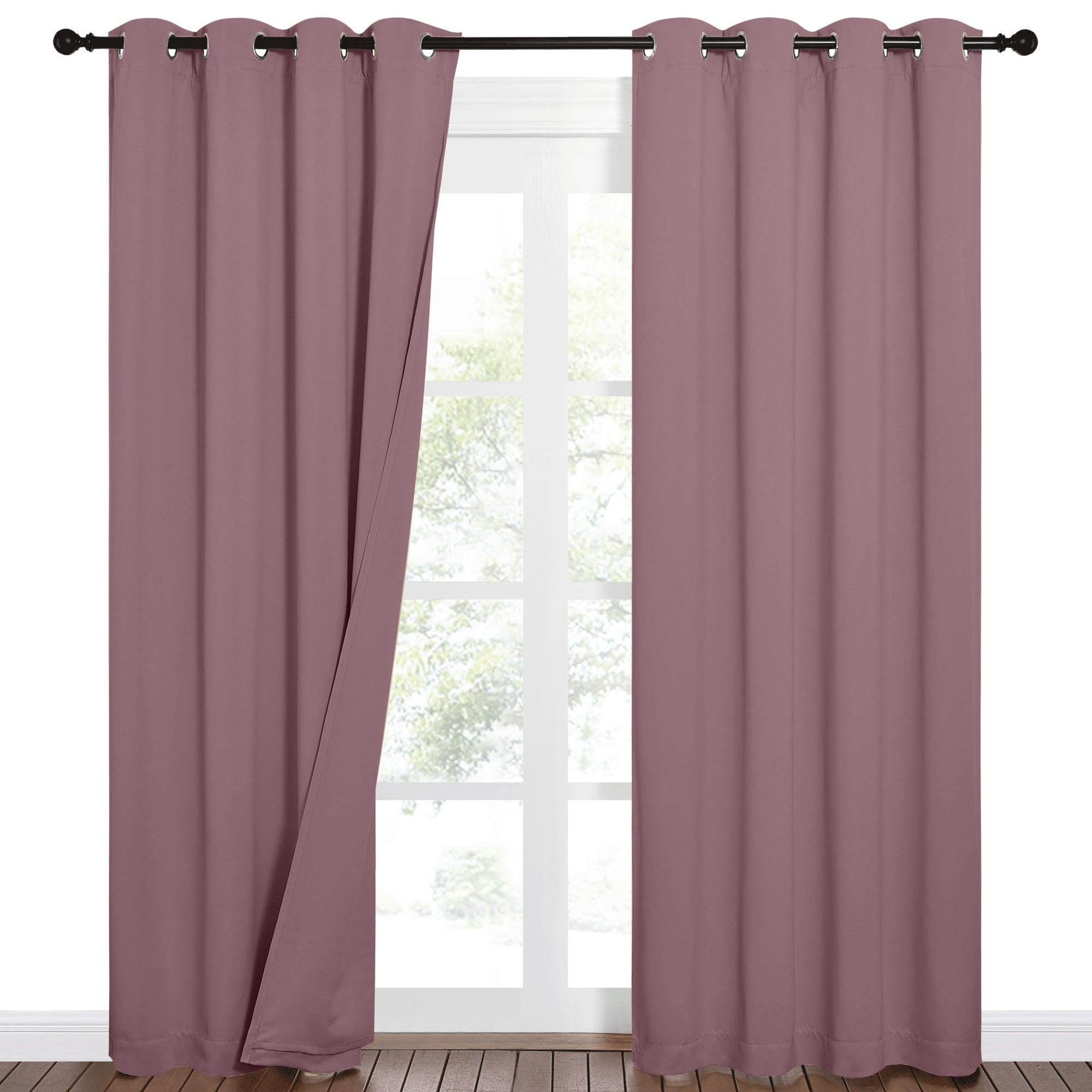 Plum 100% blackout curtains with grommets on a dark rod, one panel drawn back slightly revealing a window with green trees.