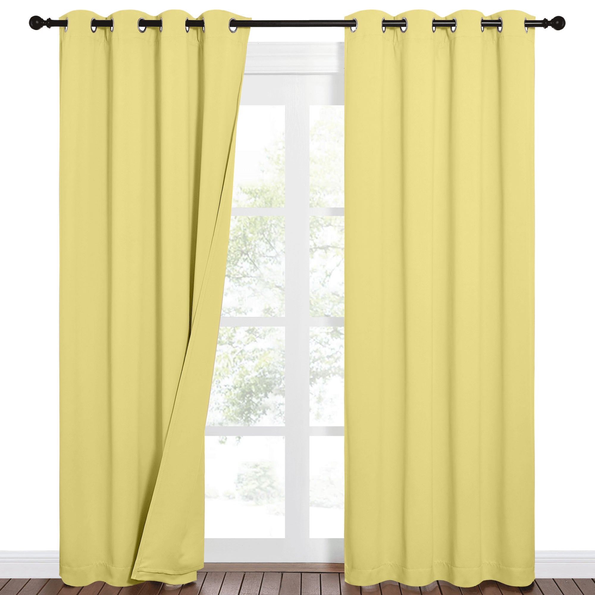 Pale yellow blackout curtains with grommets on a black rod, one panel open revealing a white window and green trees.