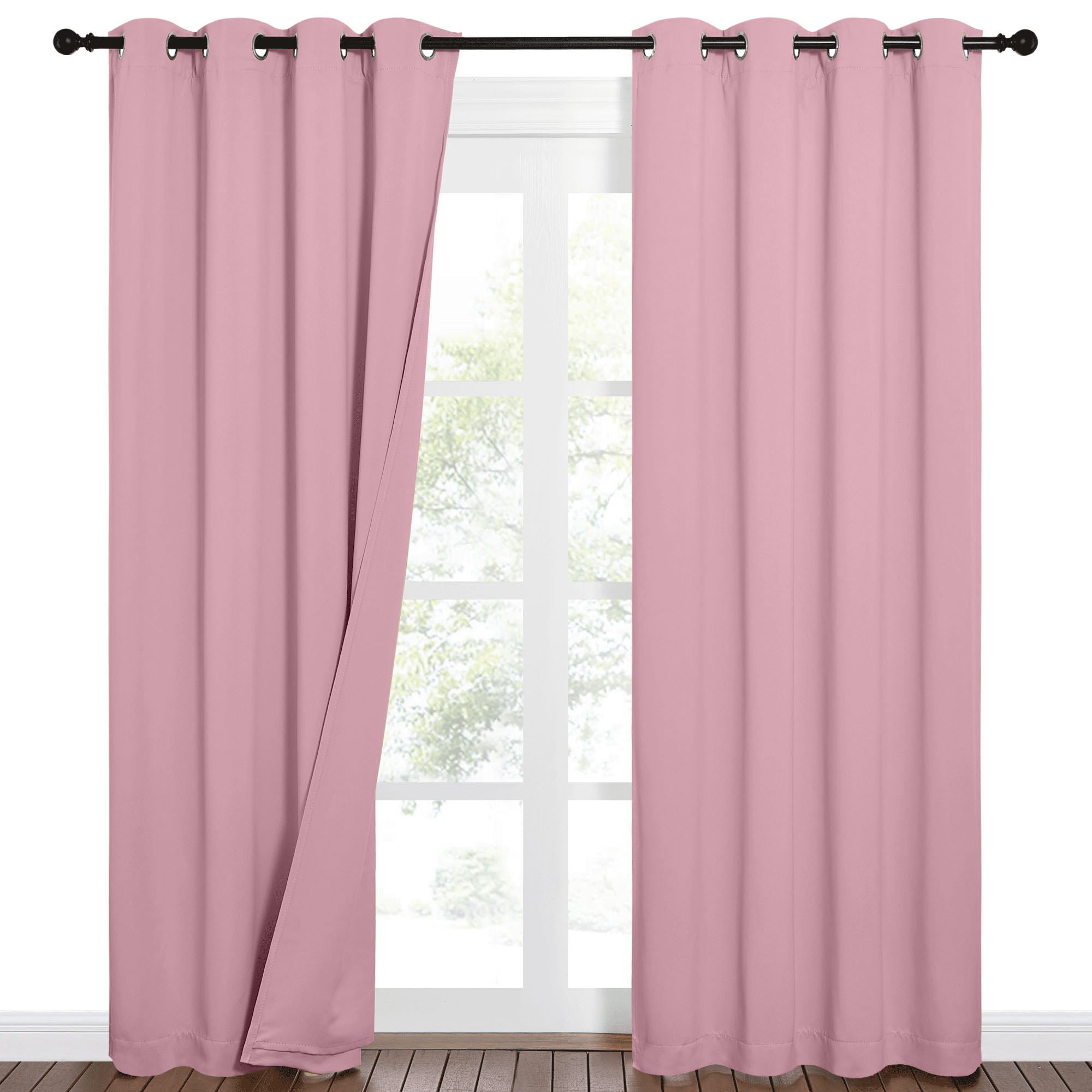 Pink sound barrier 100% blackout curtains with grommets on a rod, one panel open over a window with green trees.