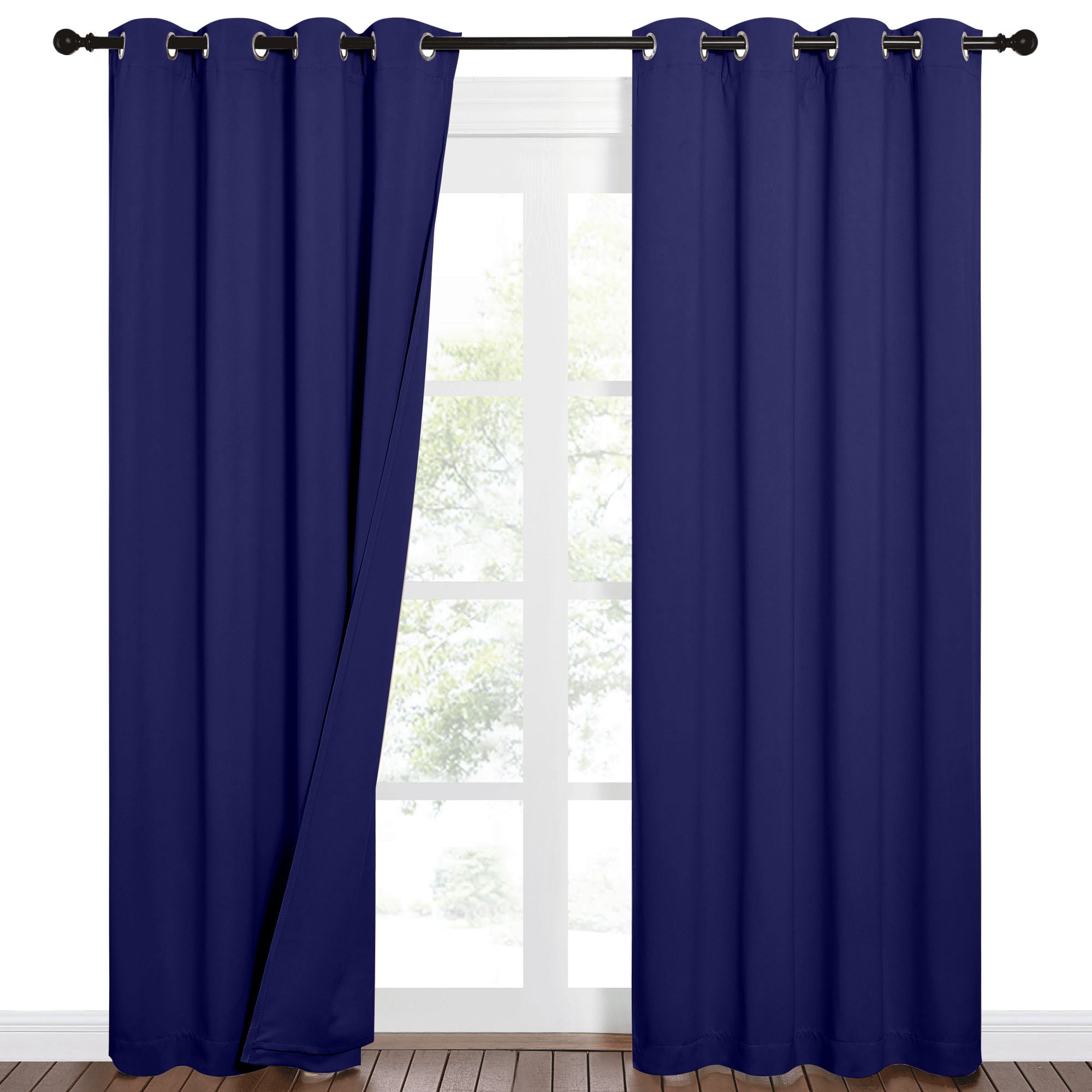 Dark blue blackout grommet curtains partially open on a window, revealing trees outside and a wooden floor.